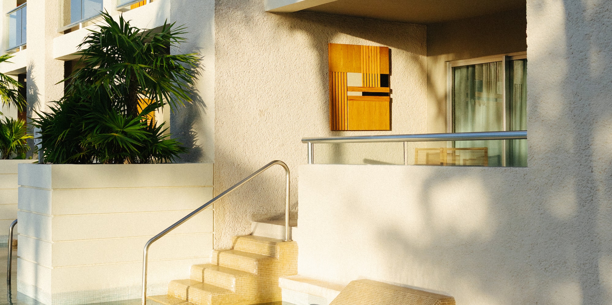 Resort building with poolside rooms, integrated steps, and sunlit balconies.