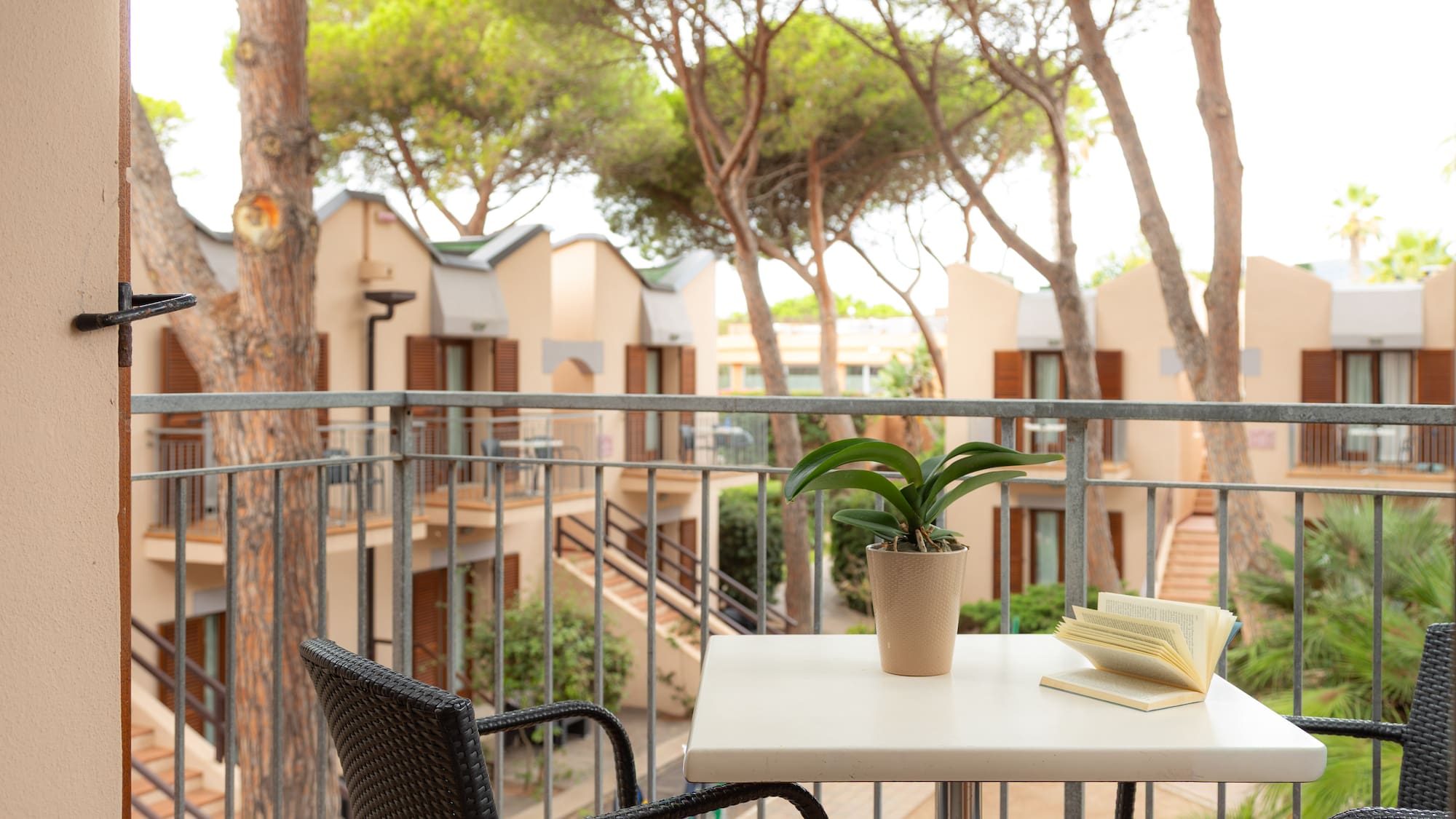 Hotel balcony with table, open book, and plant overlooking resort apartments.
