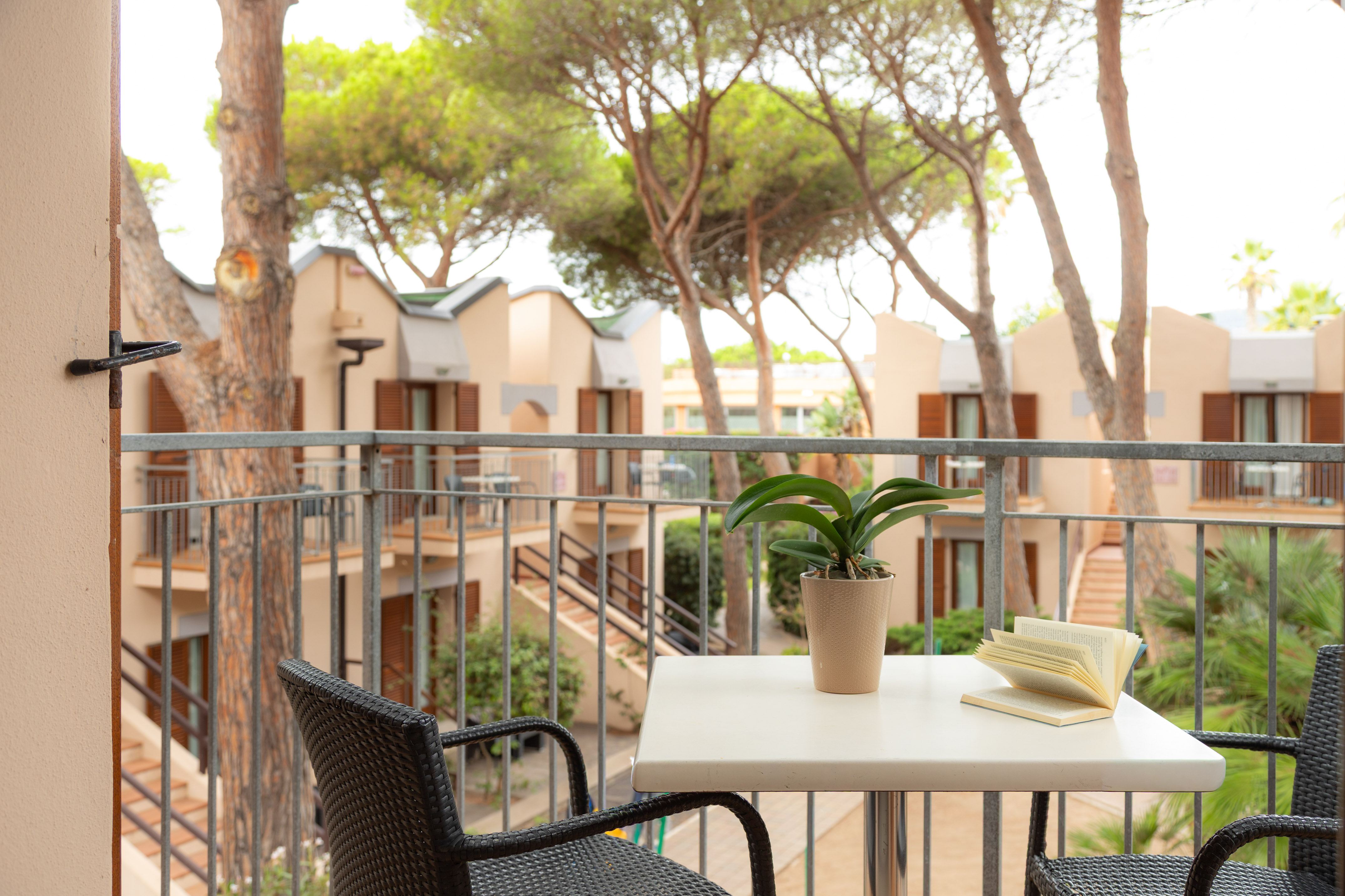 Hotel balcony with table, open book, and plant overlooking resort apartments.