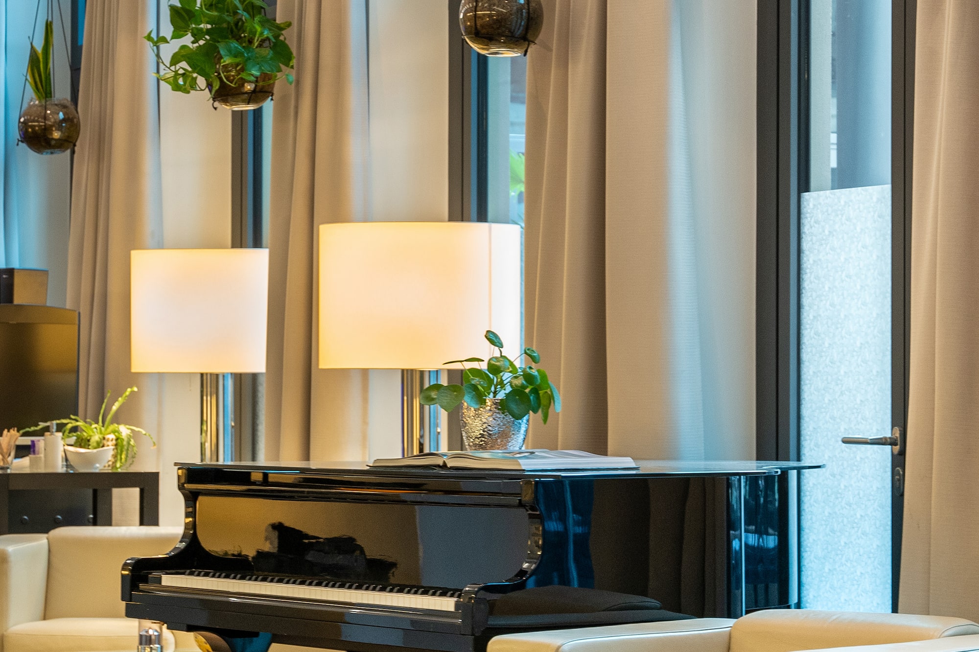 Black grand piano in modern hotel lobby with white armchairs and plants.
