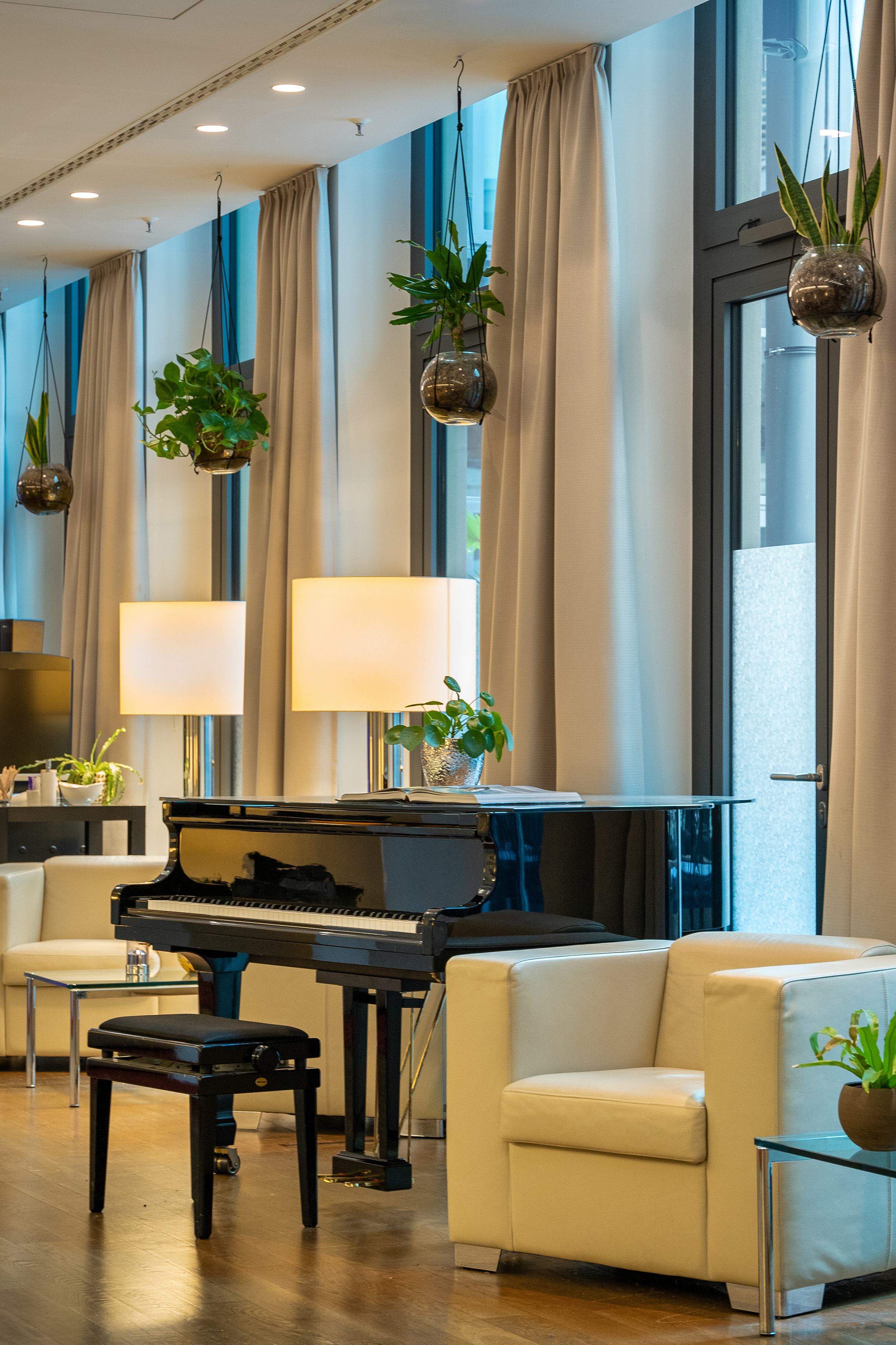 Black grand piano in modern hotel lobby with white armchairs and plants.