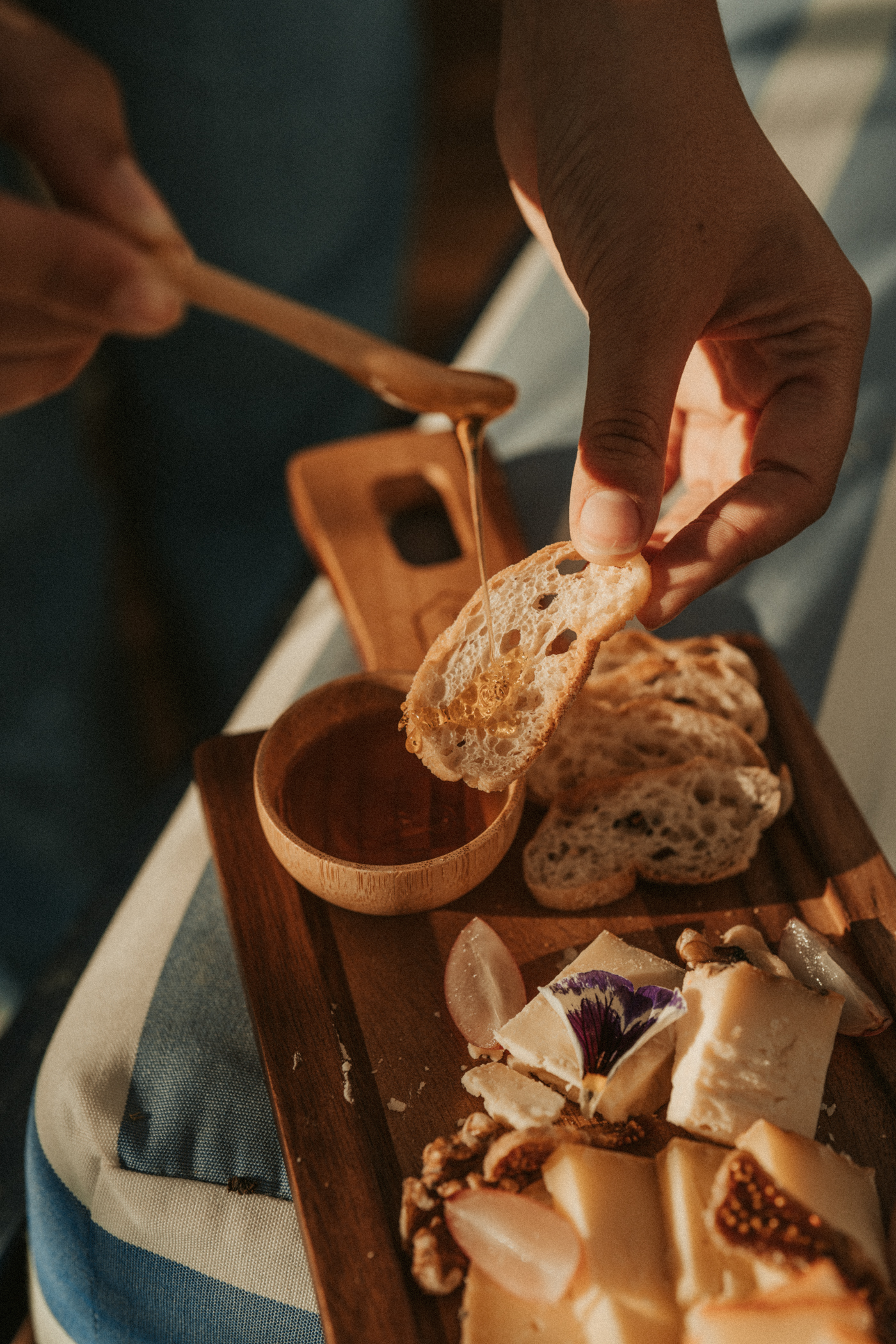 Hand drizzling honey on bread over a gourmet cheese and charcuterie board.