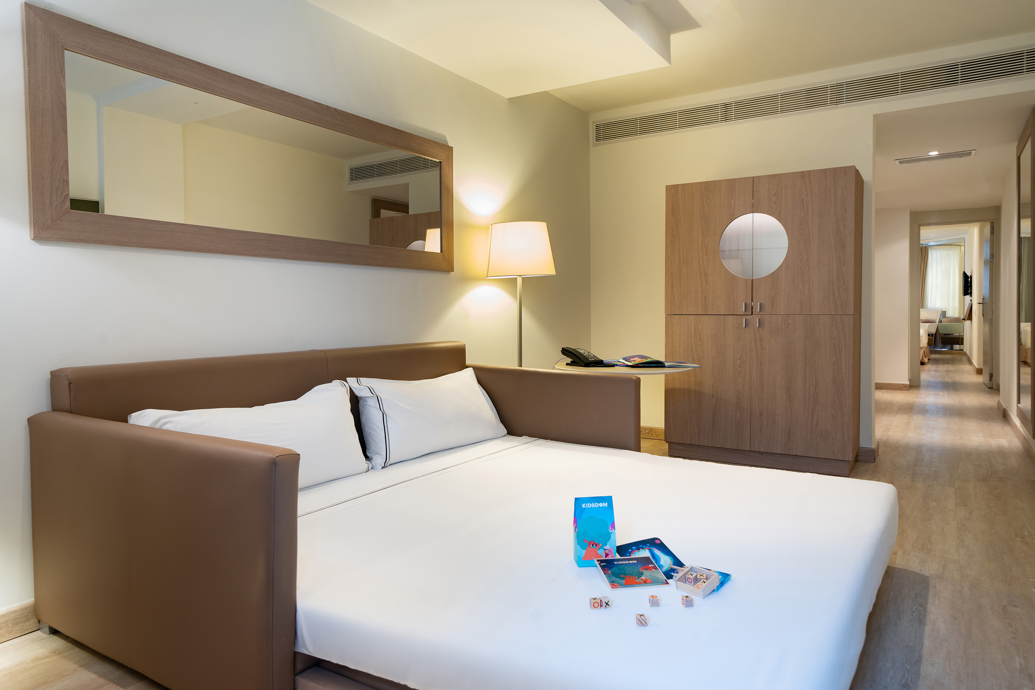 Kids-friendly hotel room with sofa bed, Kidsdom games, and wooden wardrobe.