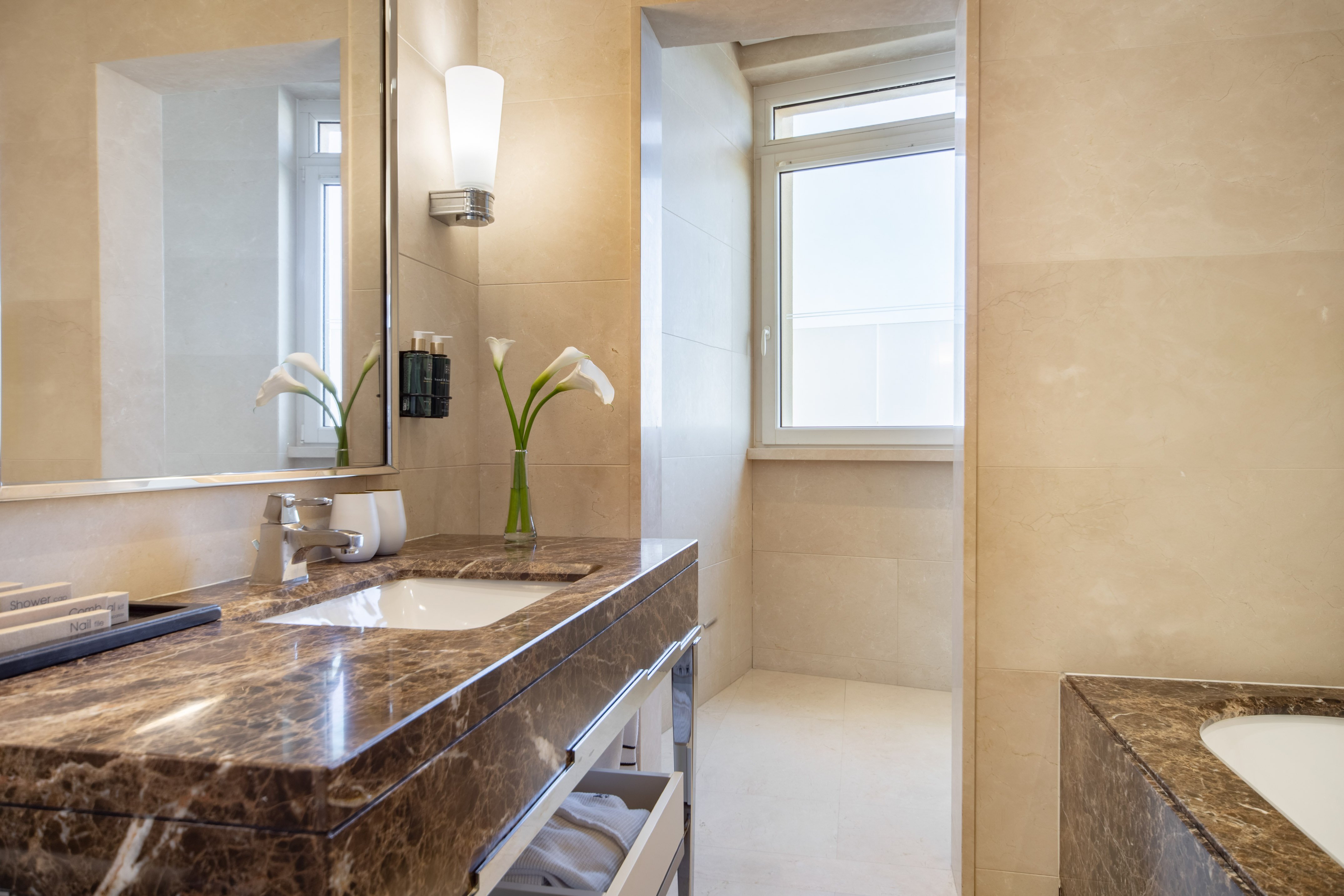 Luxury hotel bathroom with brown marble vanity, sink, large mirror, and bright window.
