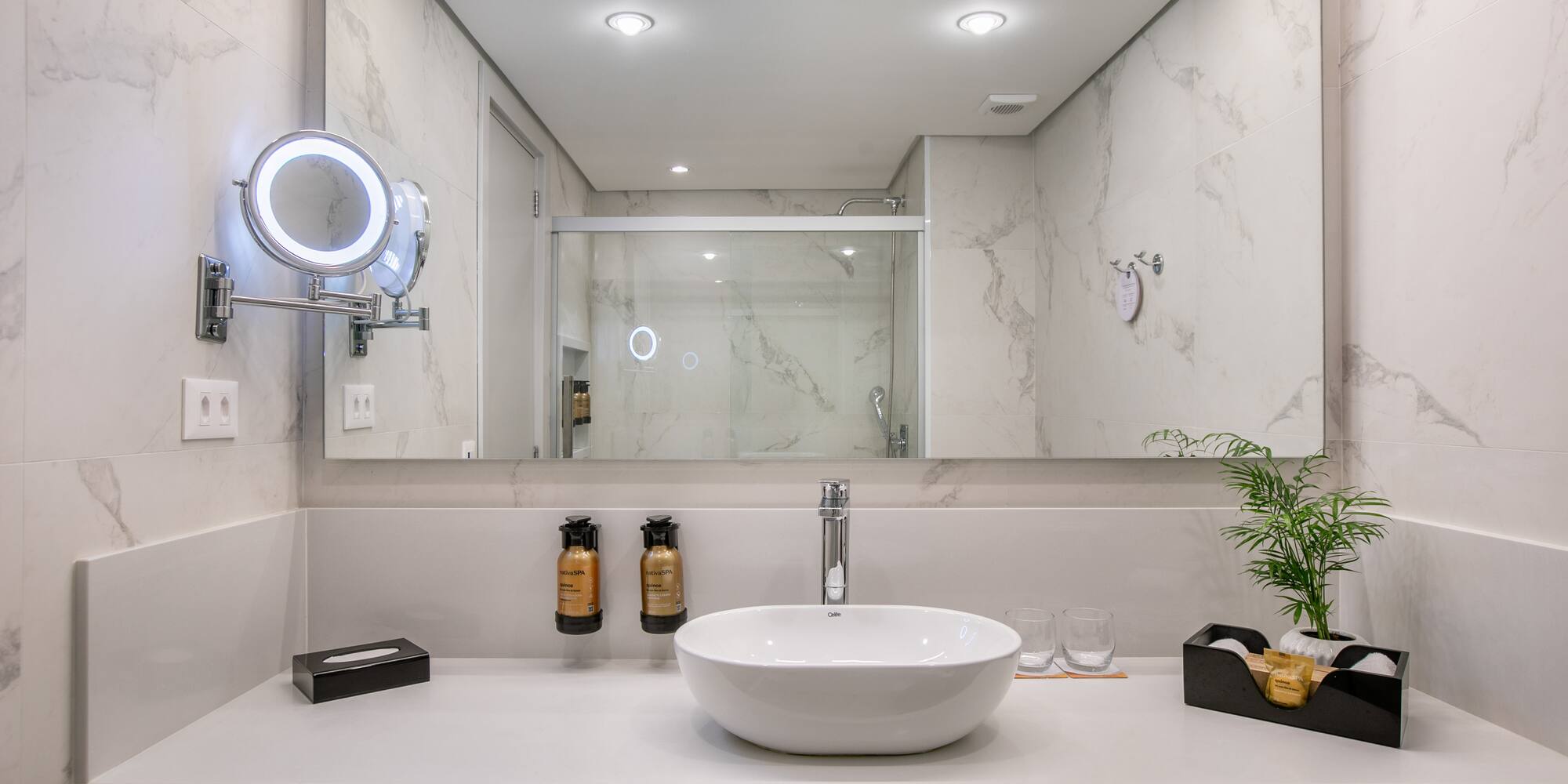 Elegant marble bathroom with vessel sink, lighted mirror, and shower view.