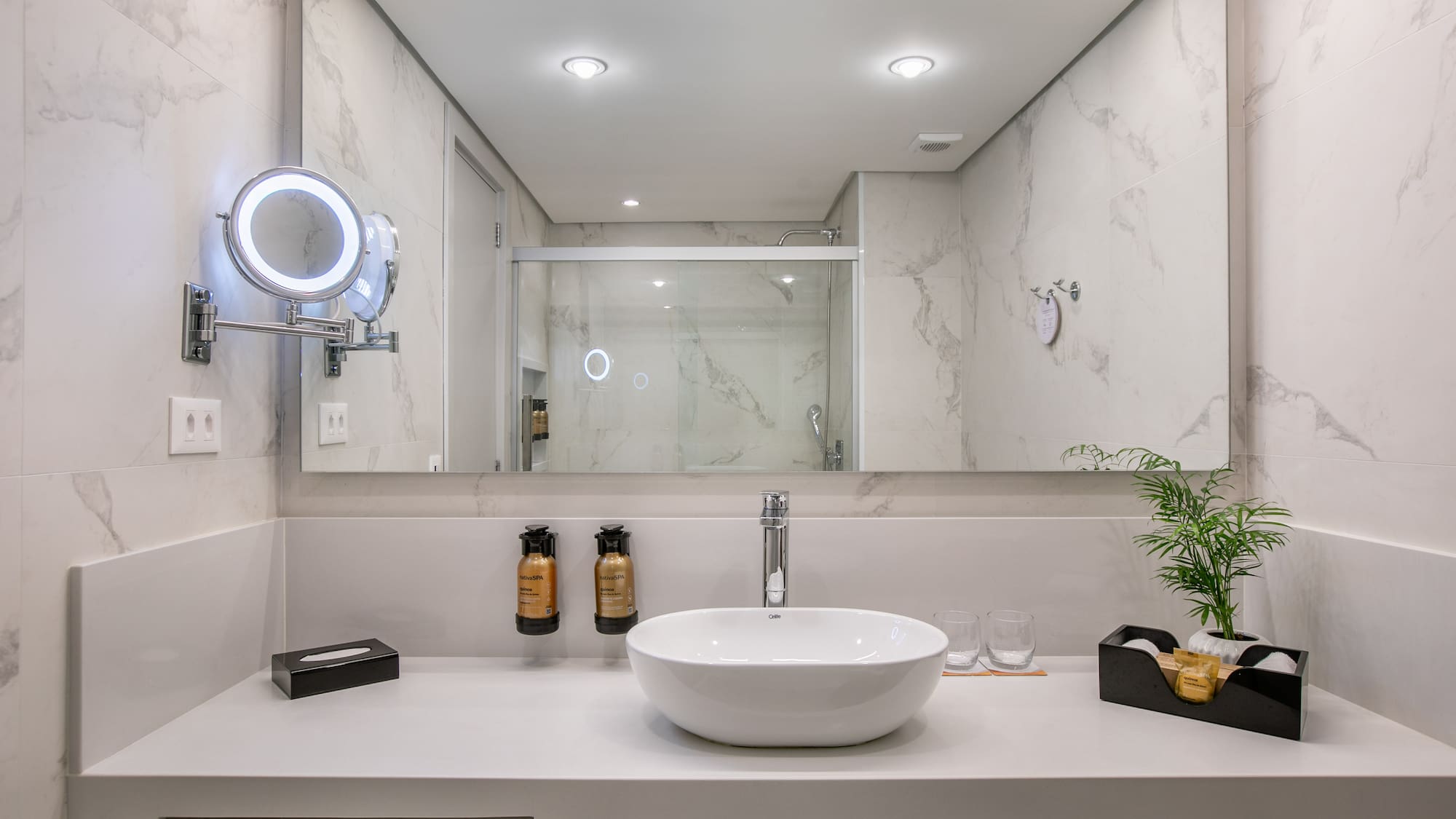 Elegant marble bathroom with vessel sink, lighted mirror, and shower view.