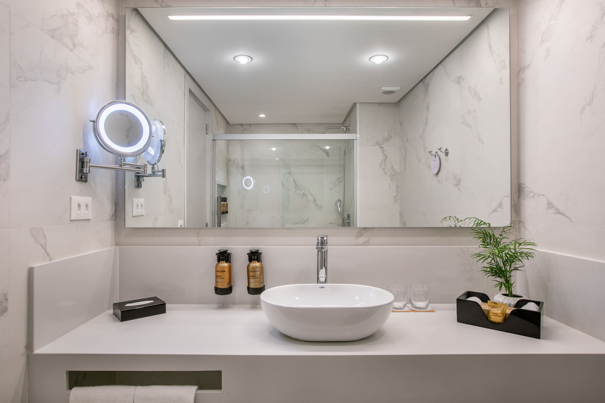 Modern white marble bathroom, vessel sink, lighted mirror, and shower reflection.