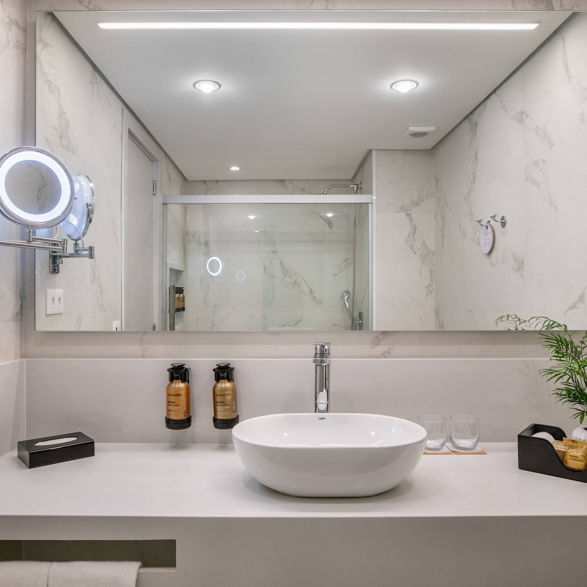 Modern white marble bathroom, vessel sink, lighted mirror, and shower reflection.