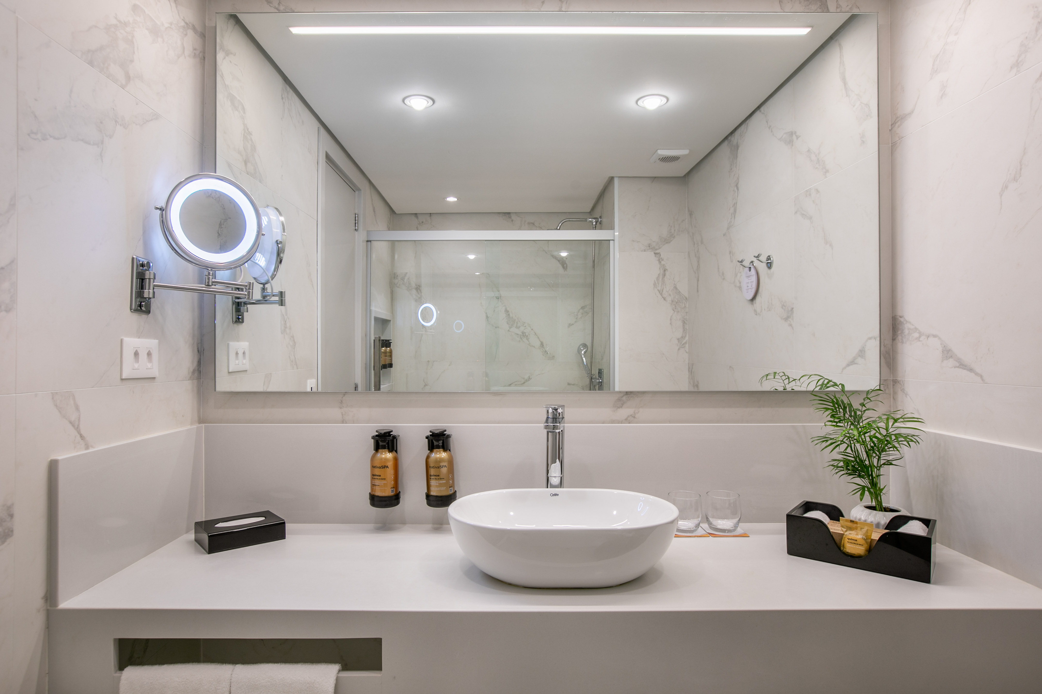 Modern white marble bathroom, vessel sink, lighted mirror, and shower reflection.