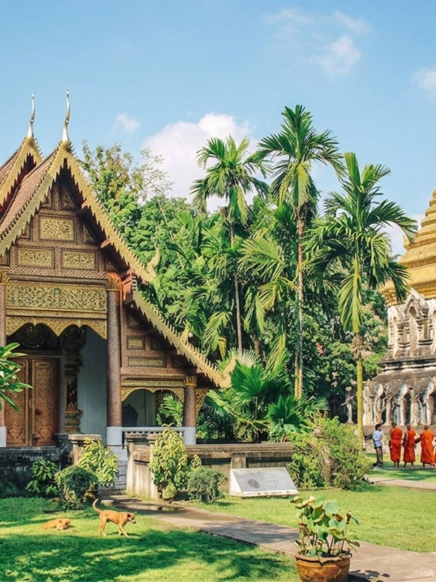Golden stupa and ornate Thai temple with monks walking in a lush garden.