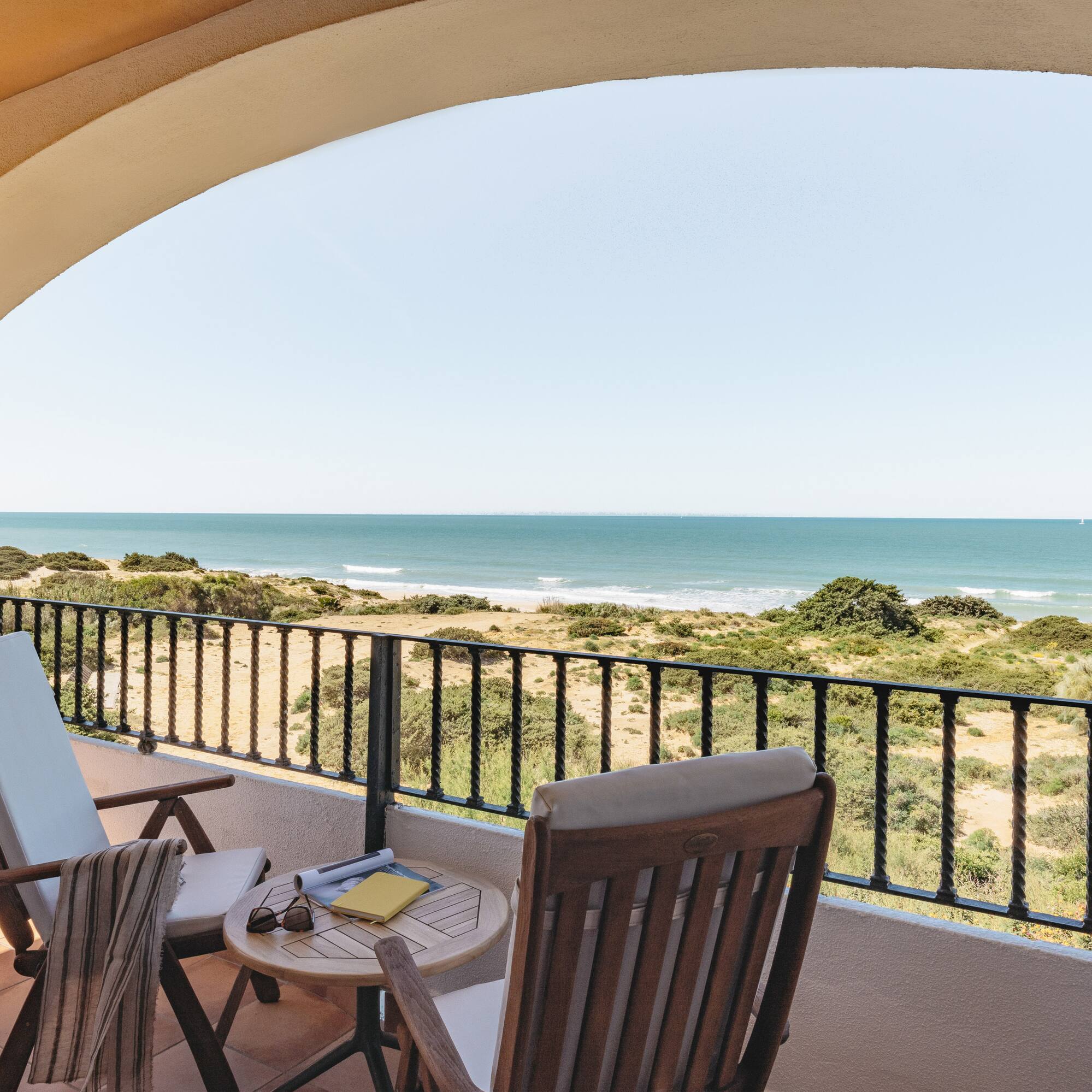 Coastal balcony with ocean view, patio furniture, and sandy dunes.