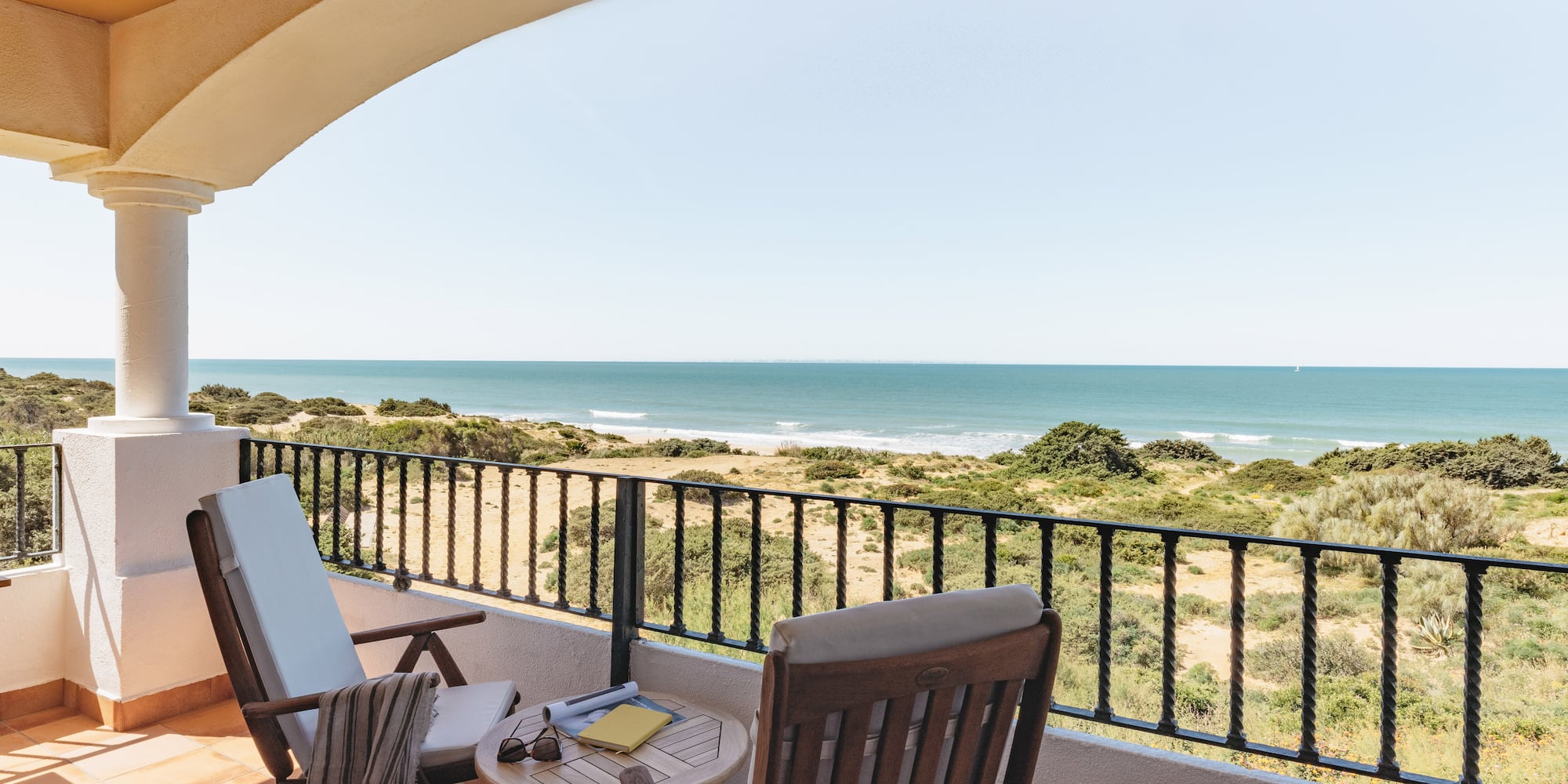 Coastal balcony with ocean view, patio furniture, and sandy dunes.