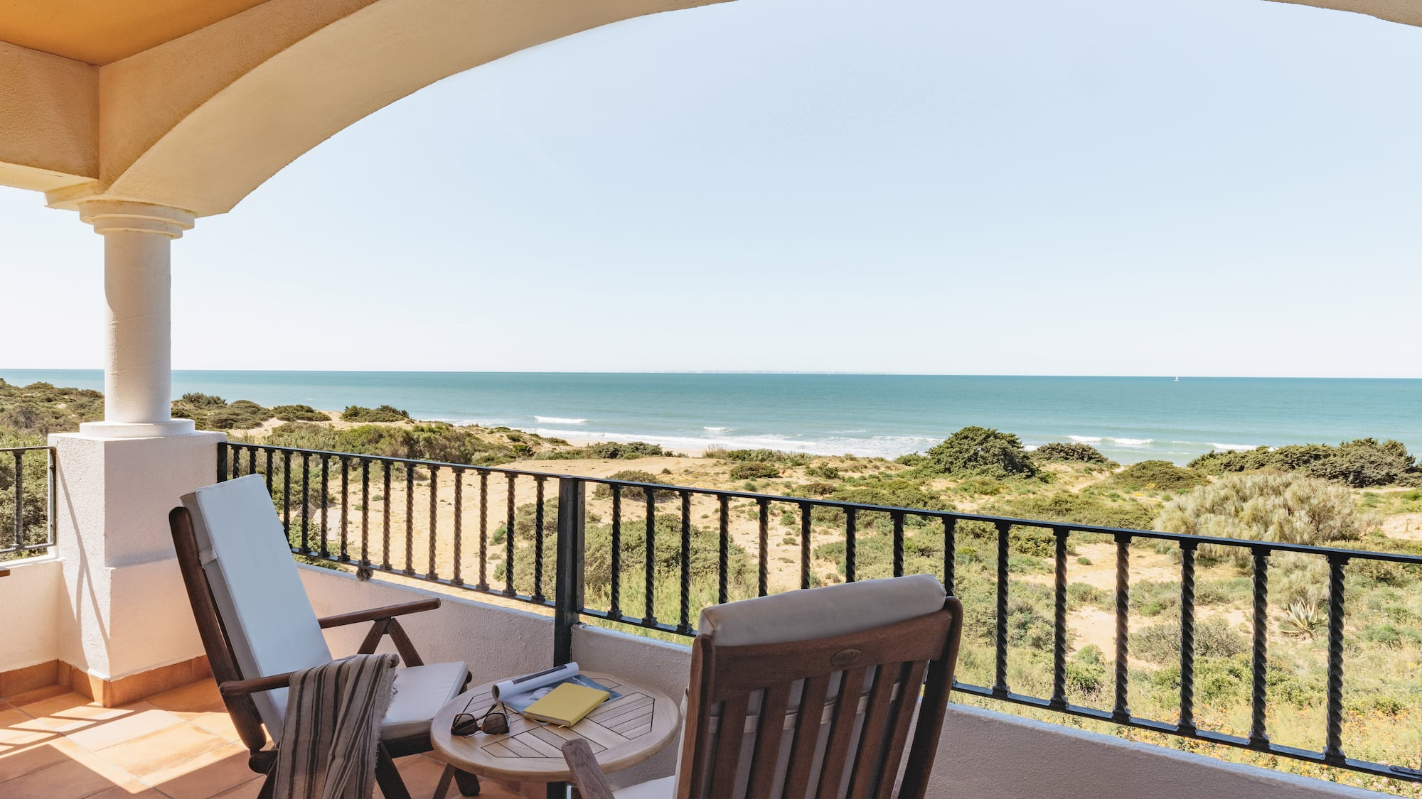 Coastal balcony with ocean view, patio furniture, and sandy dunes.