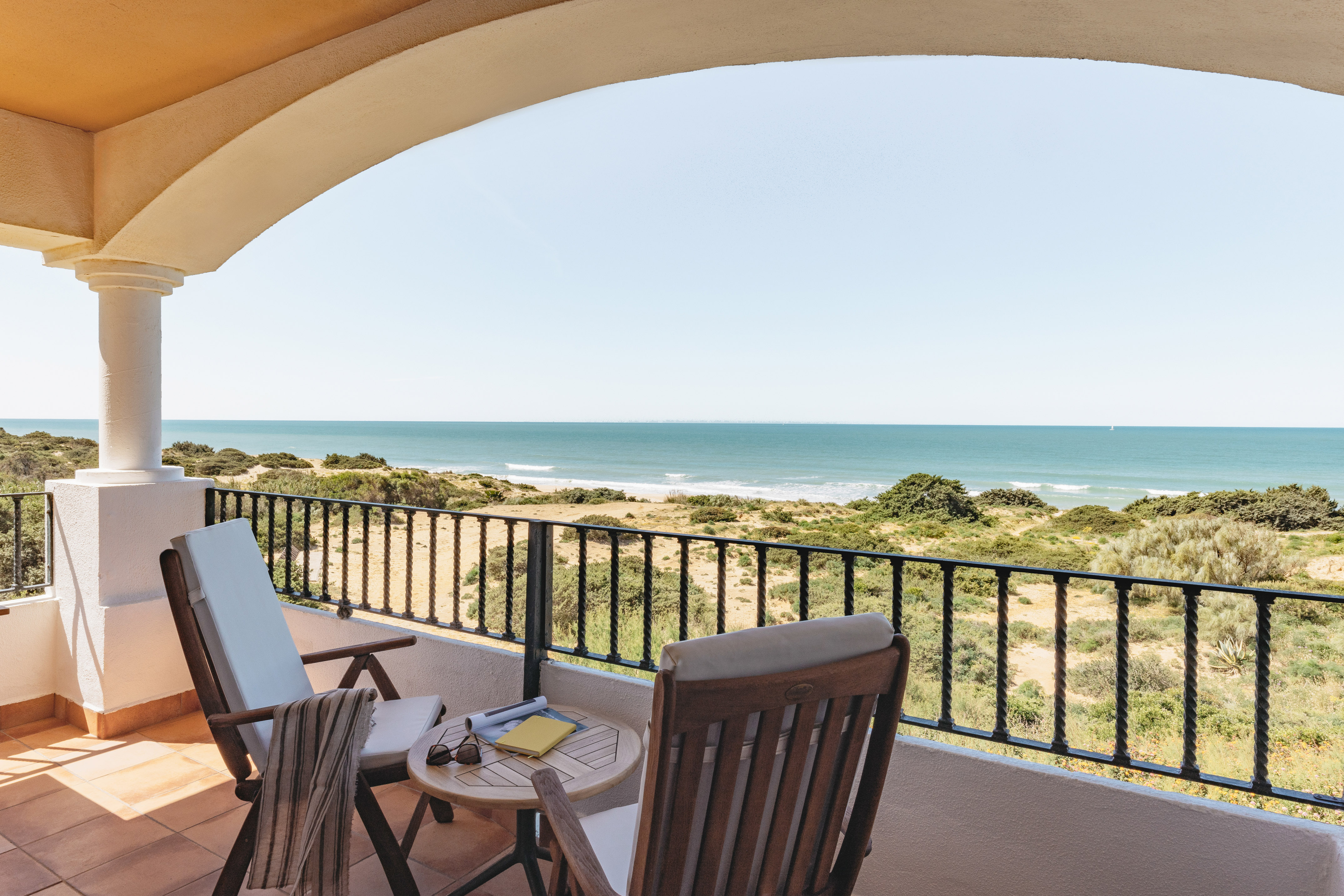 Coastal balcony with ocean view, patio furniture, and sandy dunes.