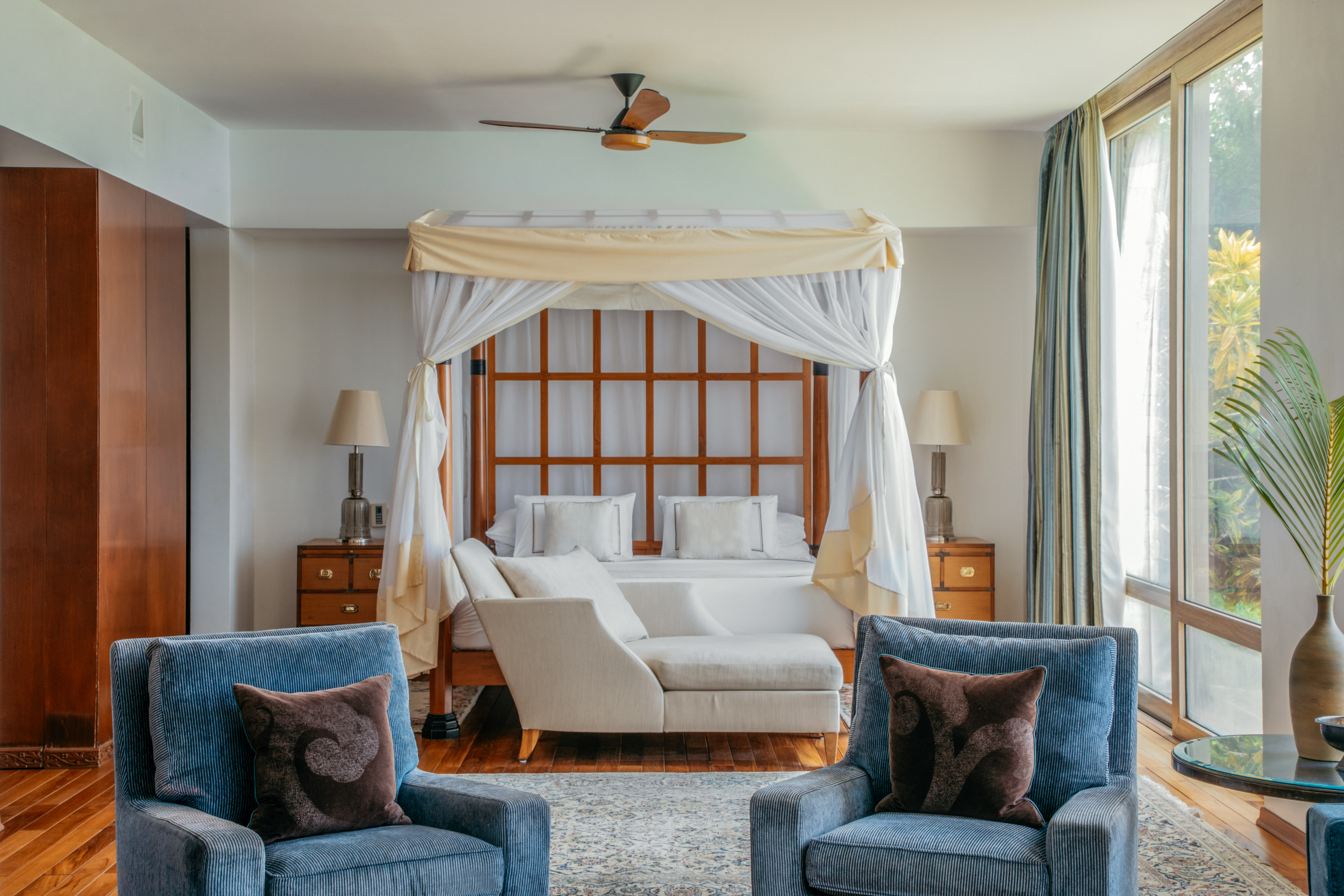 Luxurious bedroom: Four-poster canopy bed, blue armchairs, bright window.