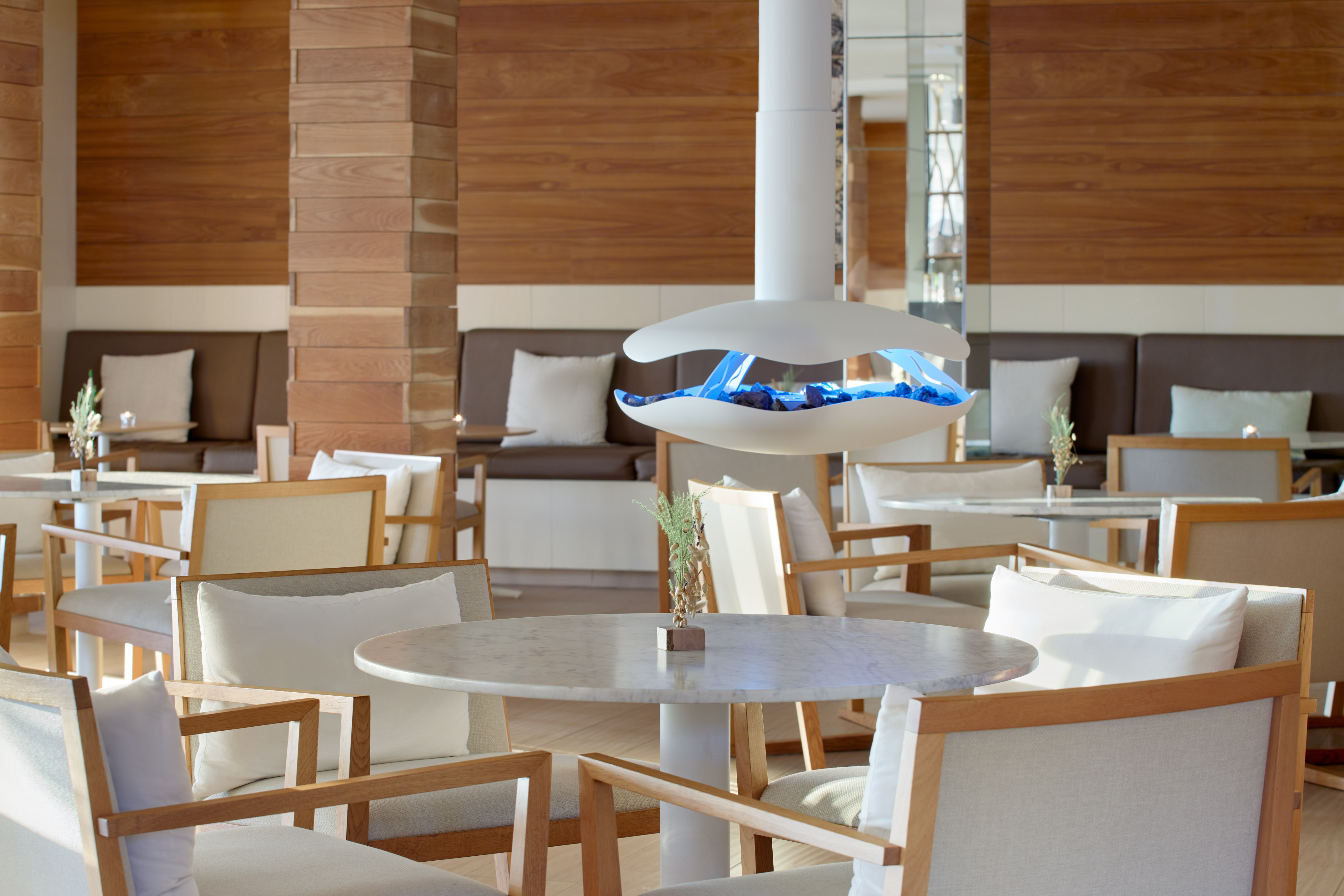 Modern lounge with wood paneling, white seating, and blue flame fireplace.