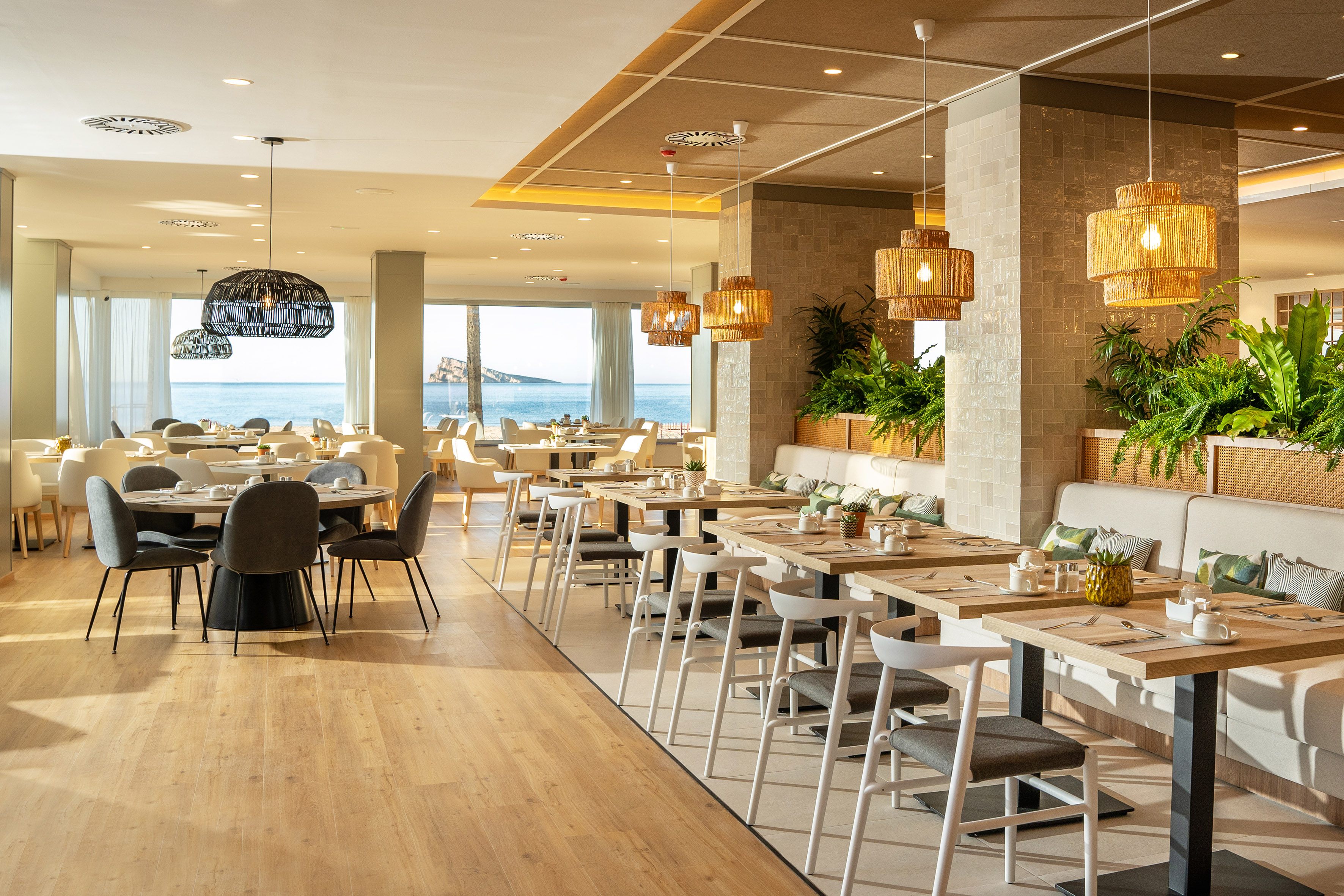 Elegant beachfront restaurant with ocean views, modern tables, and rattan lighting.