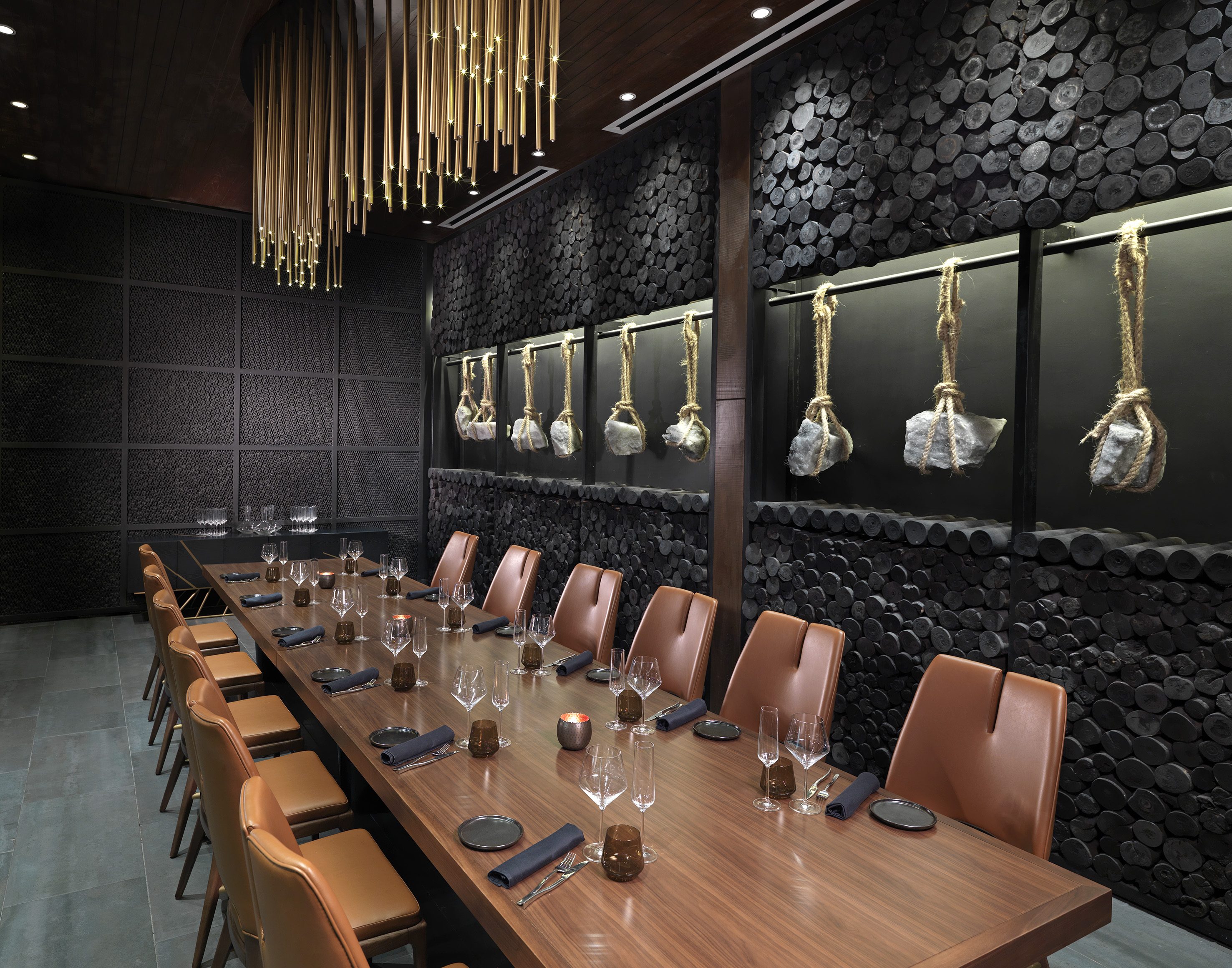 Modern private dining room with dark log walls, gold chandelier, and long dining table.