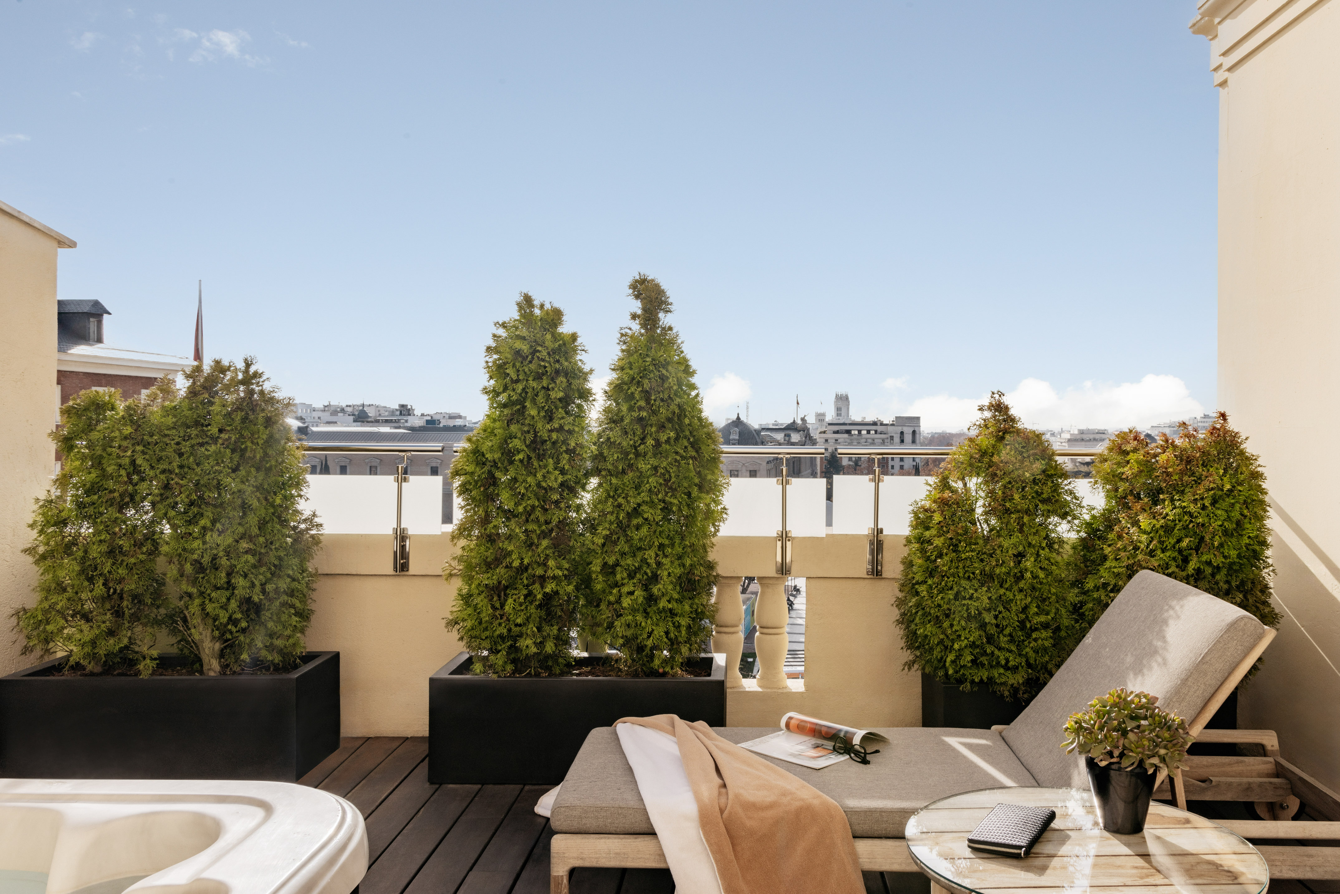 Rooftop terrace with city view, lounge chair, potted trees, and hot tub.