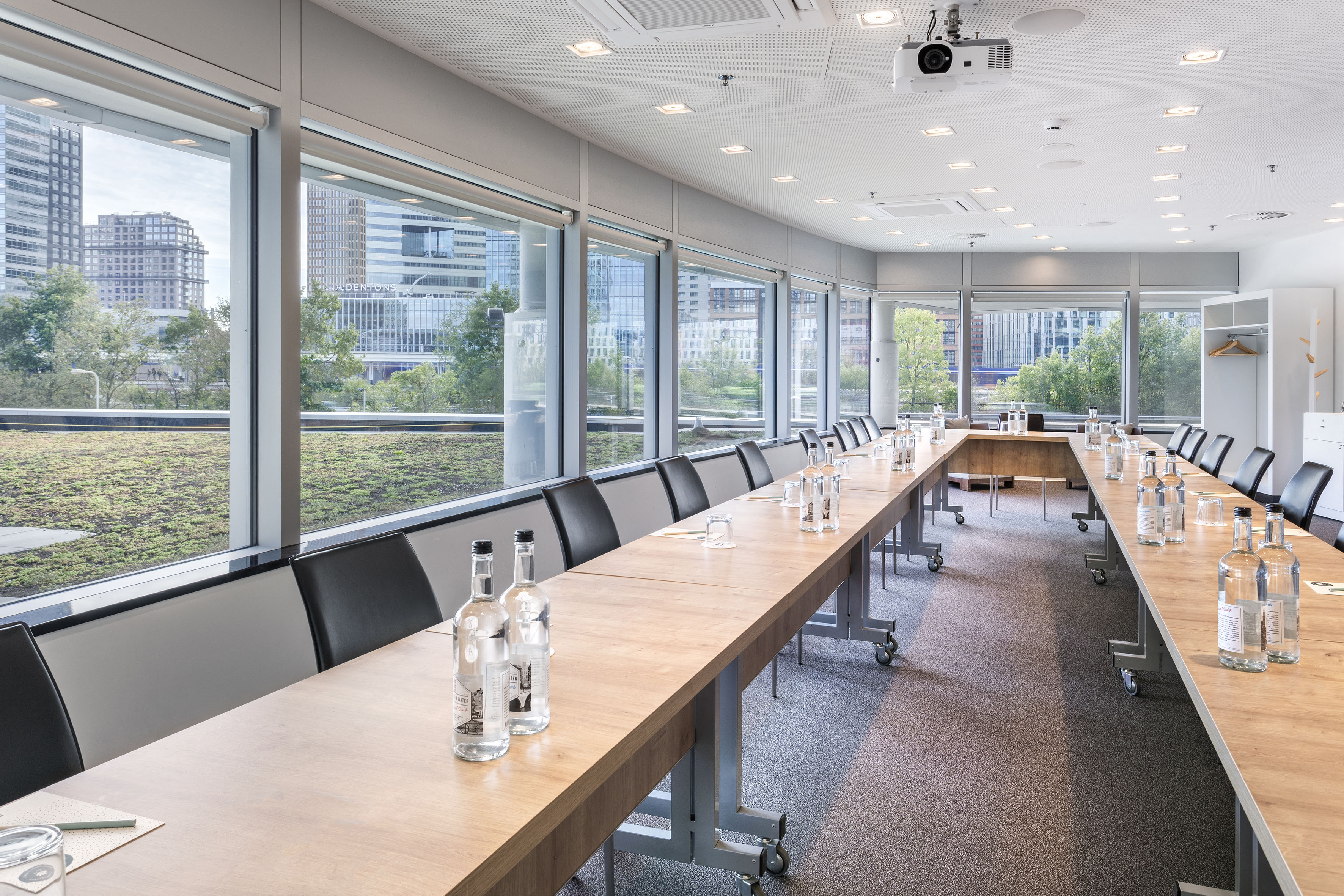 Modern meeting room with U-shaped table setup, city view, and green rooftop.