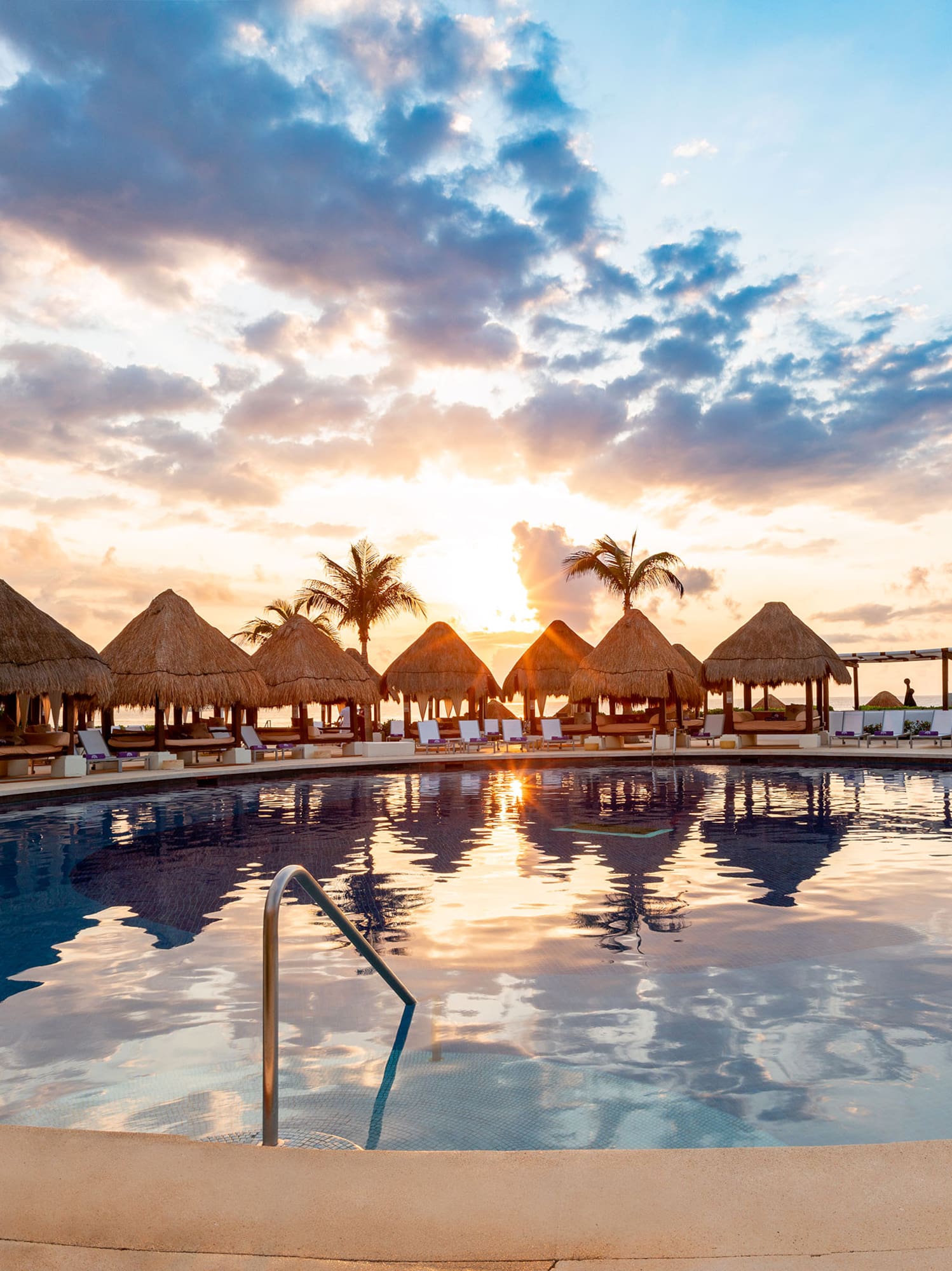 a pool with straw umbrellas and a beach in the background