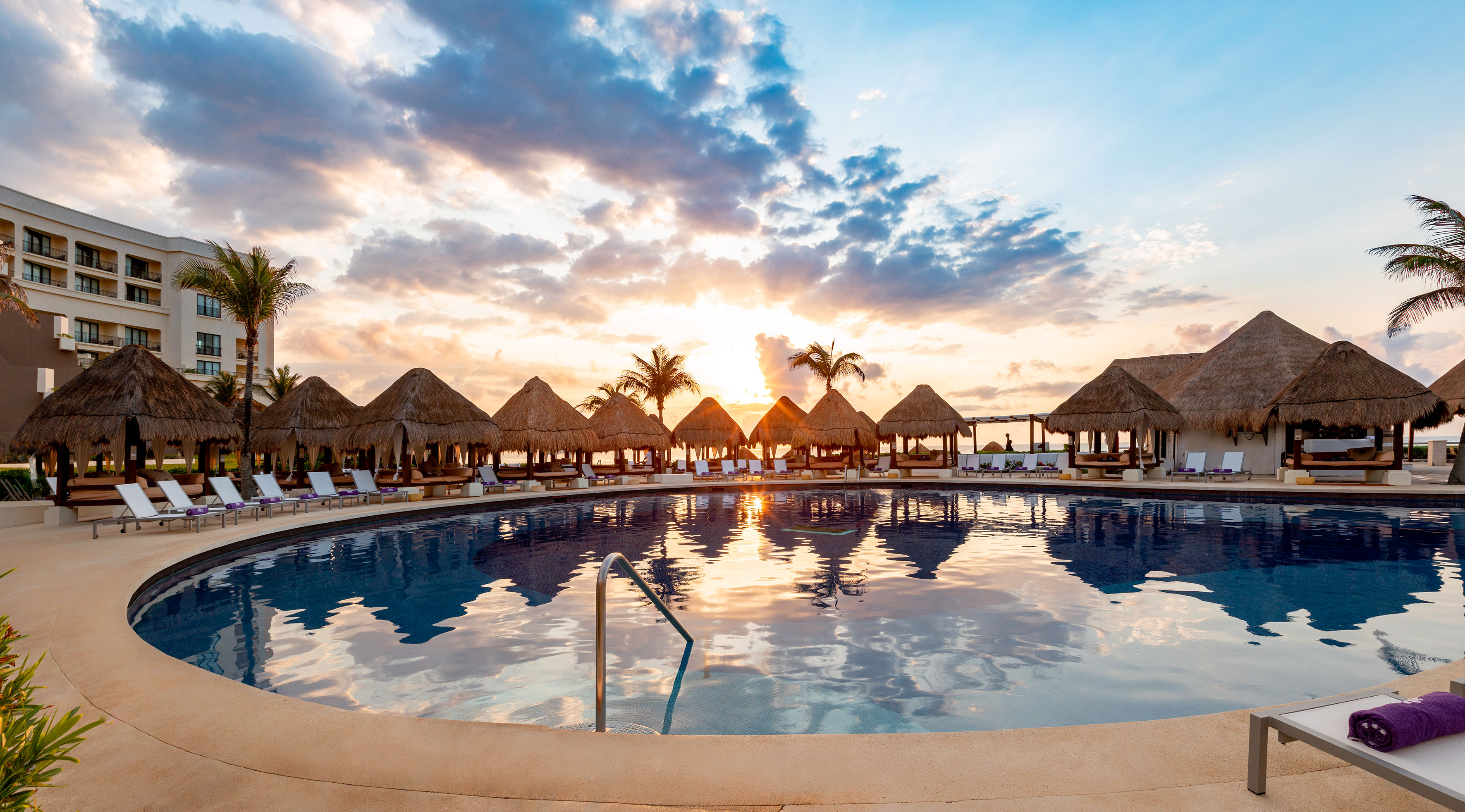a pool with straw umbrellas and a beach in the background