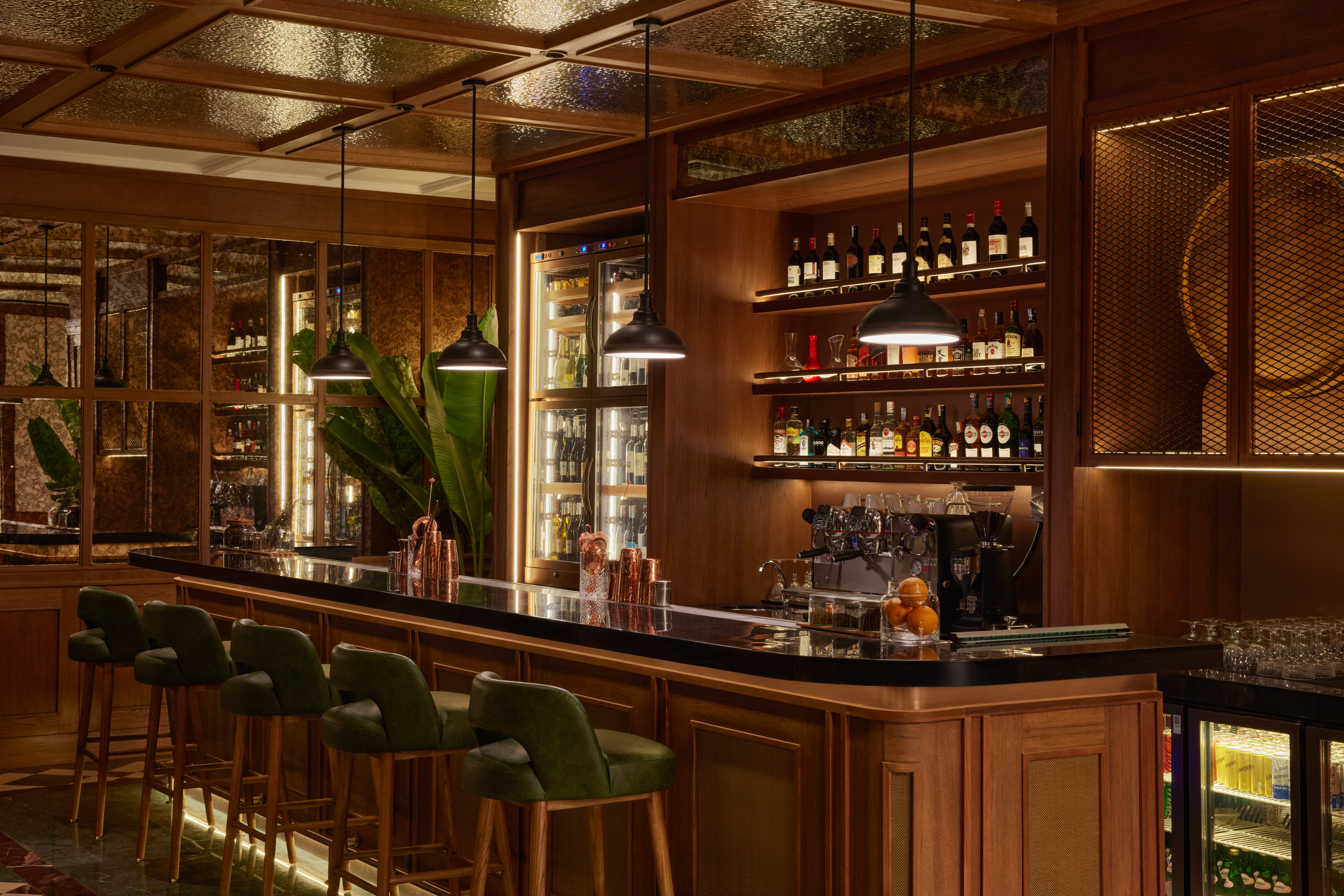 Upscale bar with dark wood, green stools, and lit liquor display.