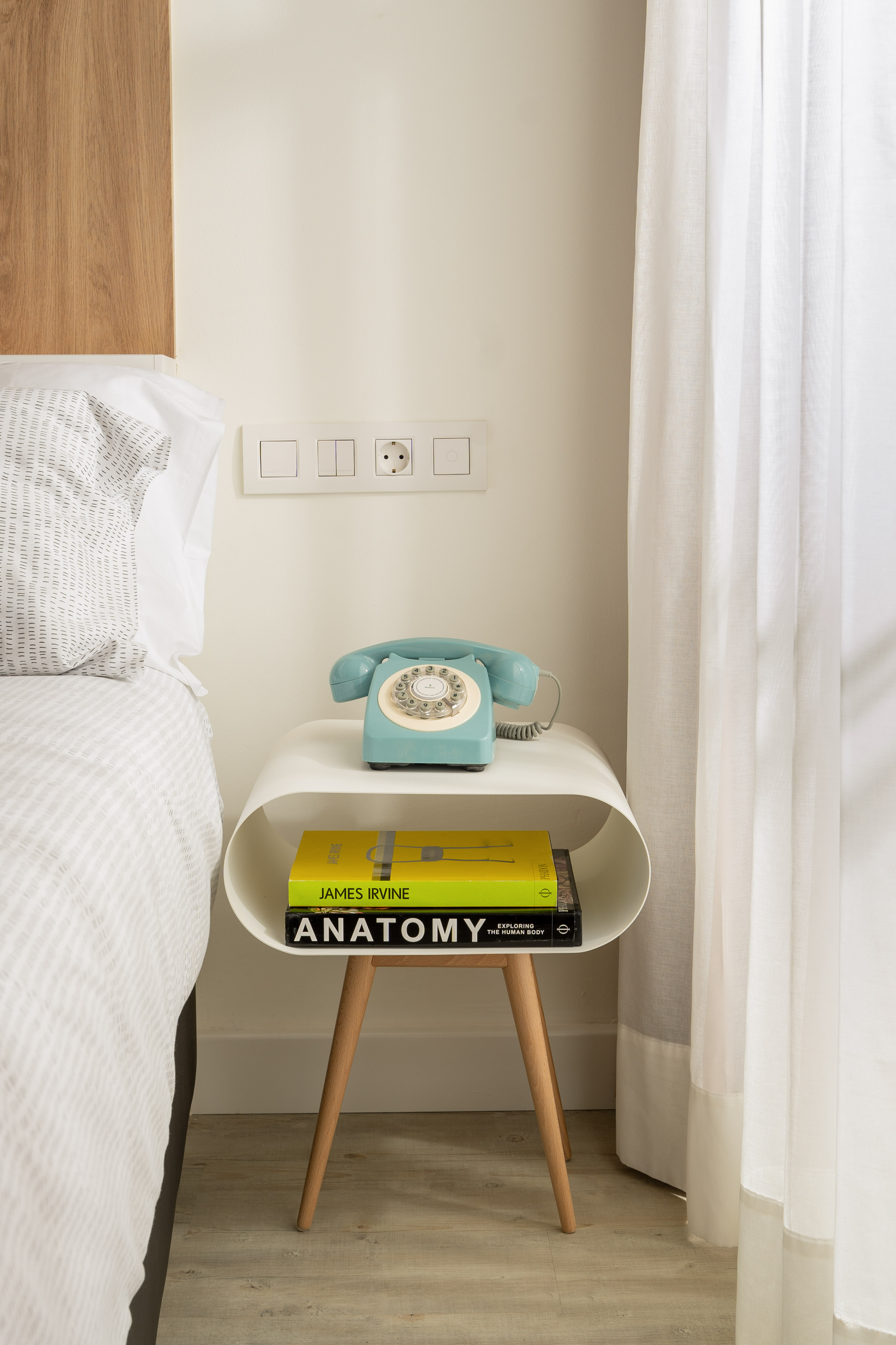 Modern bedroom: white bedside table, vintage blue rotary phone, and books.