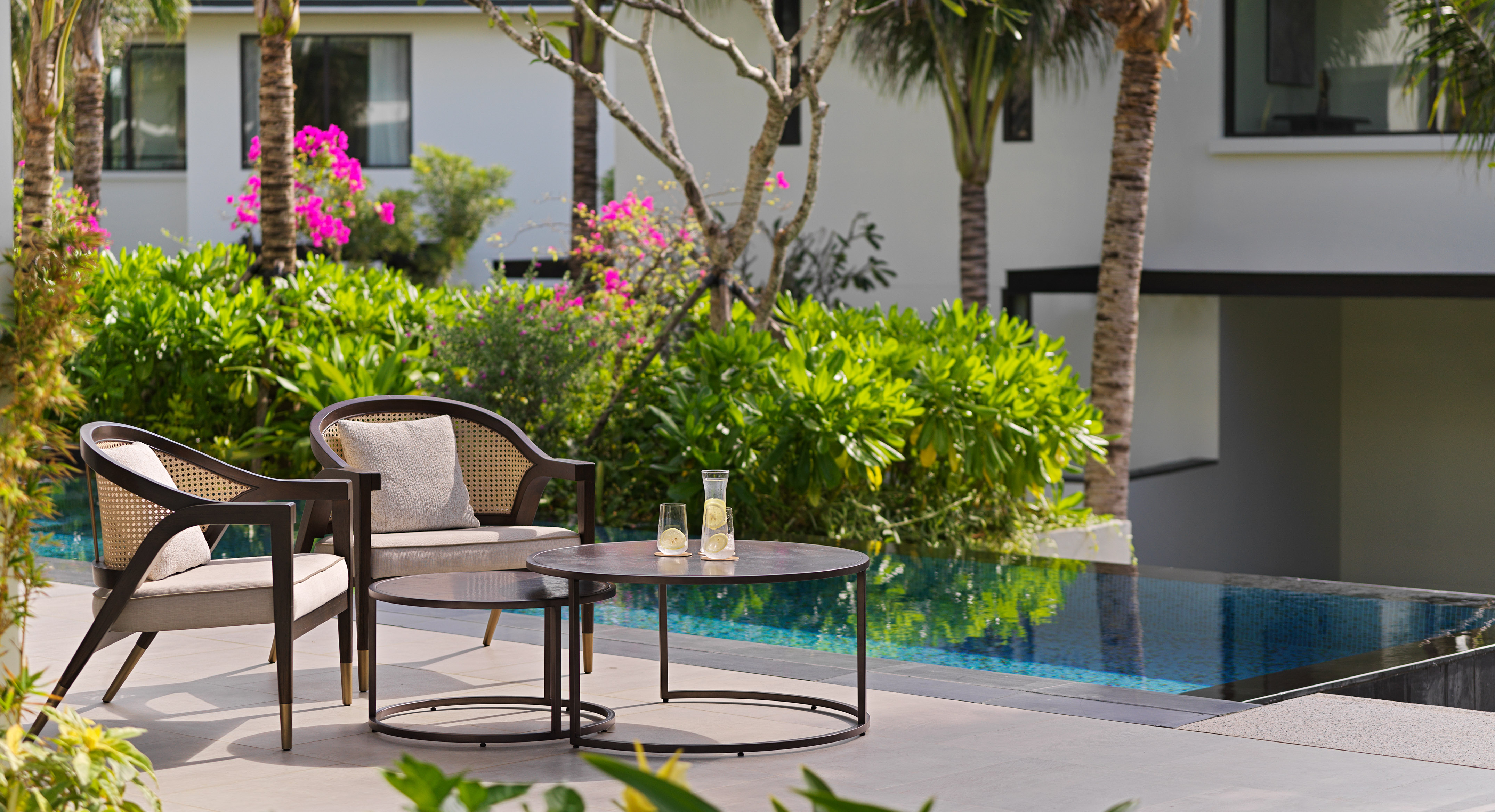 Outdoor lounge chairs and coffee tables by a resort pool with lush garden.