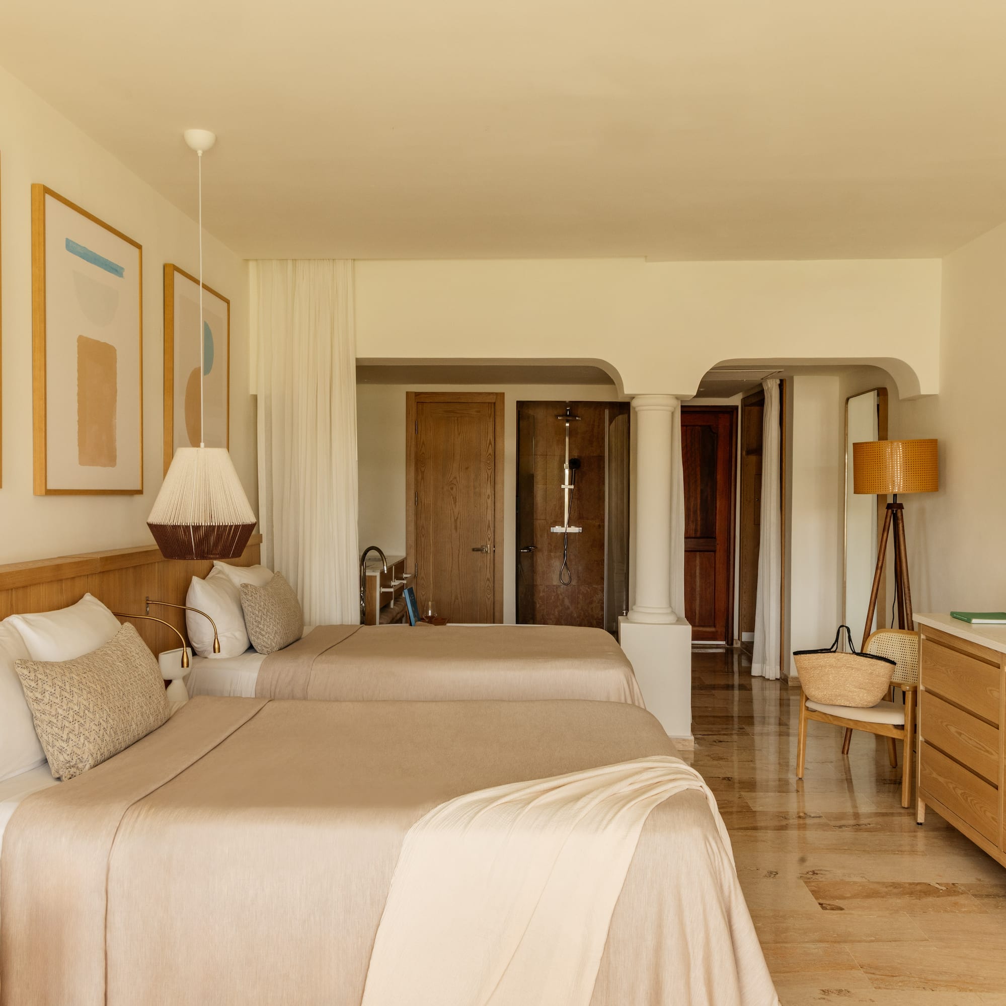 Minimalist resort bedroom with two beds, light wood furniture, and abstract art.