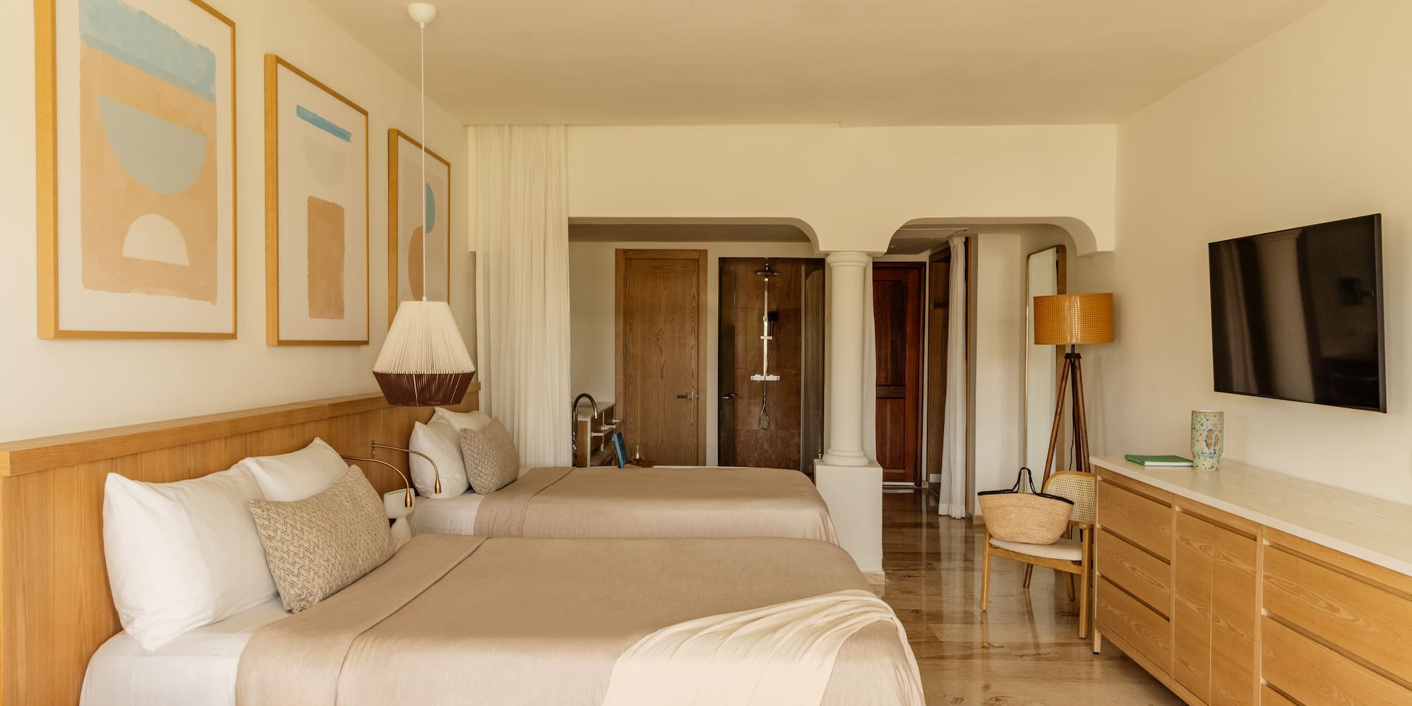 Minimalist resort bedroom with two beds, light wood furniture, and abstract art.