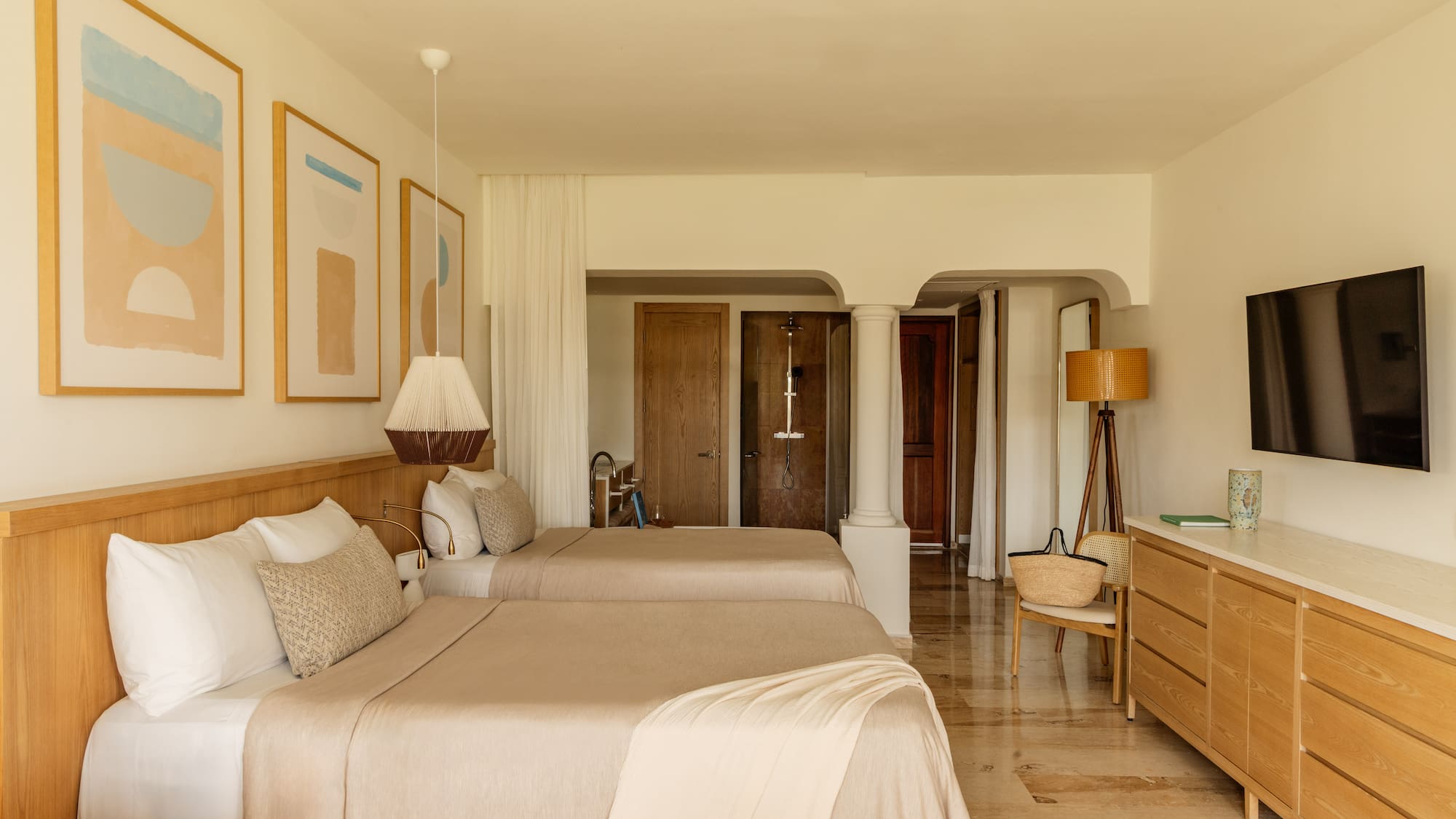 Minimalist resort bedroom with two beds, light wood furniture, and abstract art.