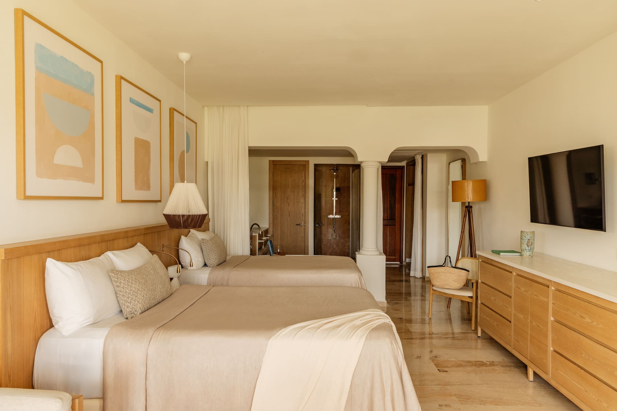 Minimalist resort bedroom with two beds, light wood furniture, and abstract art.