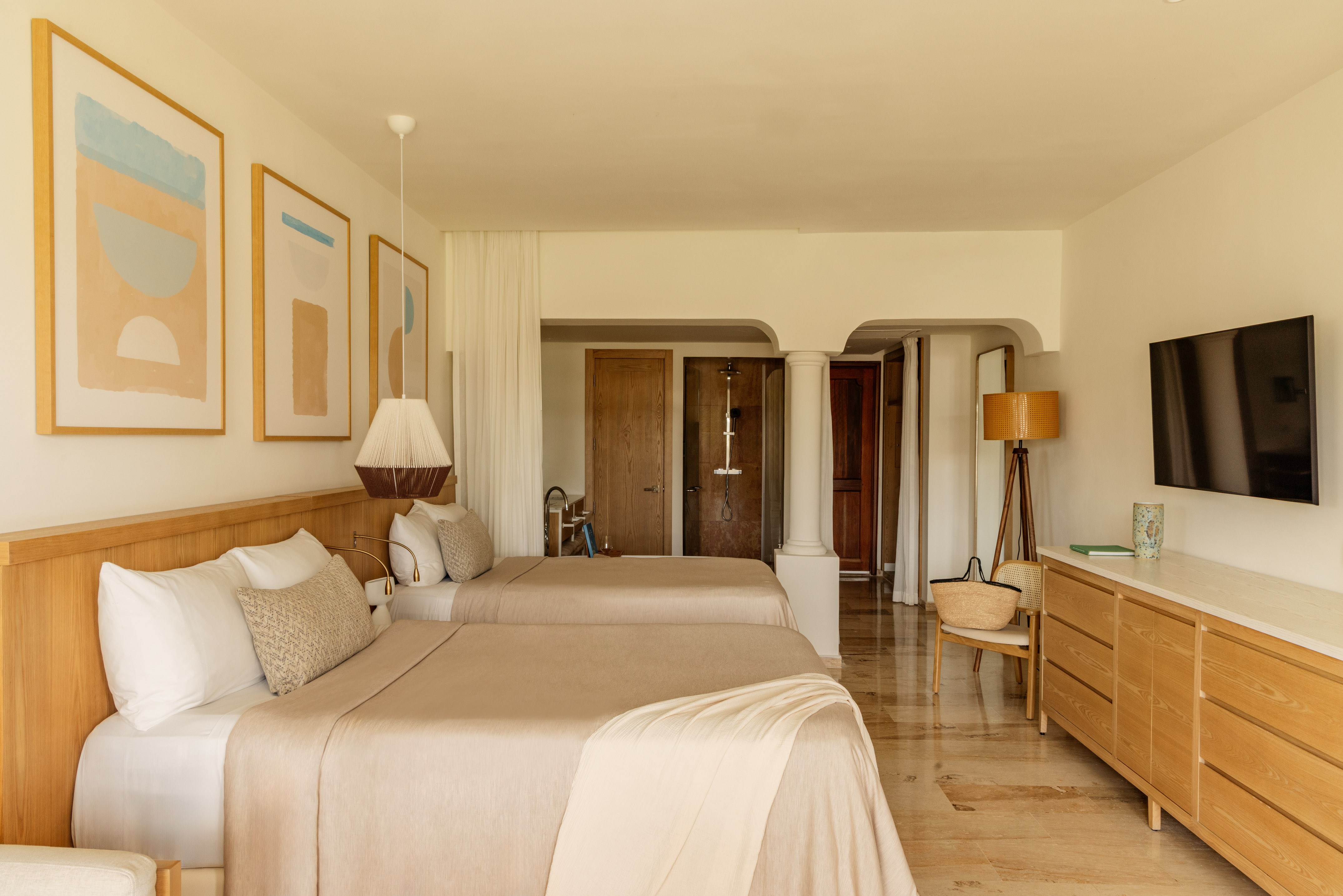 Minimalist resort bedroom with two beds, light wood furniture, and abstract art.