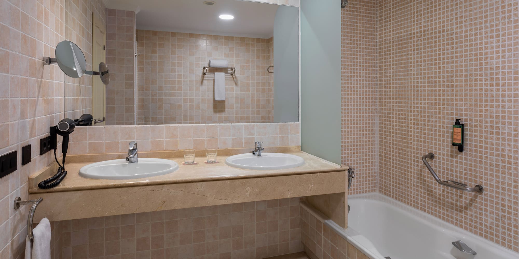 Clean tiled bathroom with double sink vanity, large mirror, and bathtub.