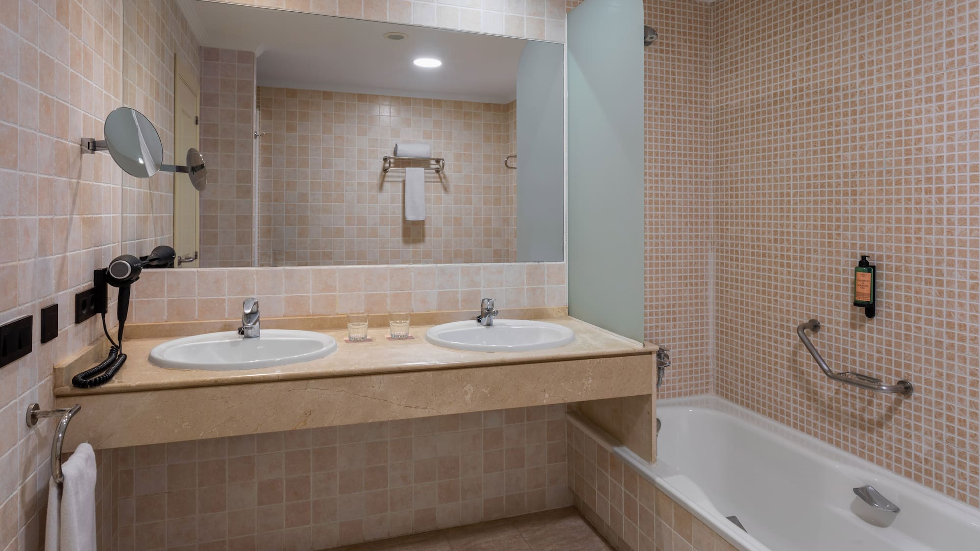 Clean tiled bathroom with double sink vanity, large mirror, and bathtub.