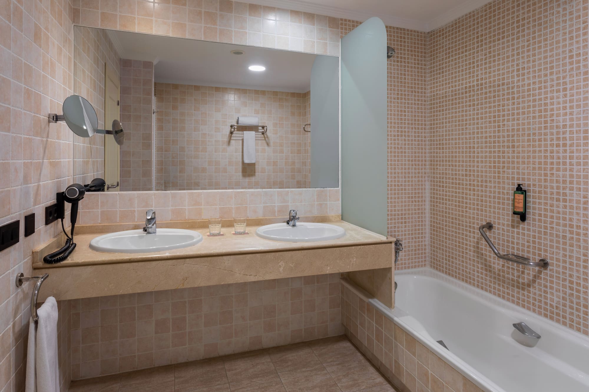 Clean tiled bathroom with double sink vanity, large mirror, and bathtub.