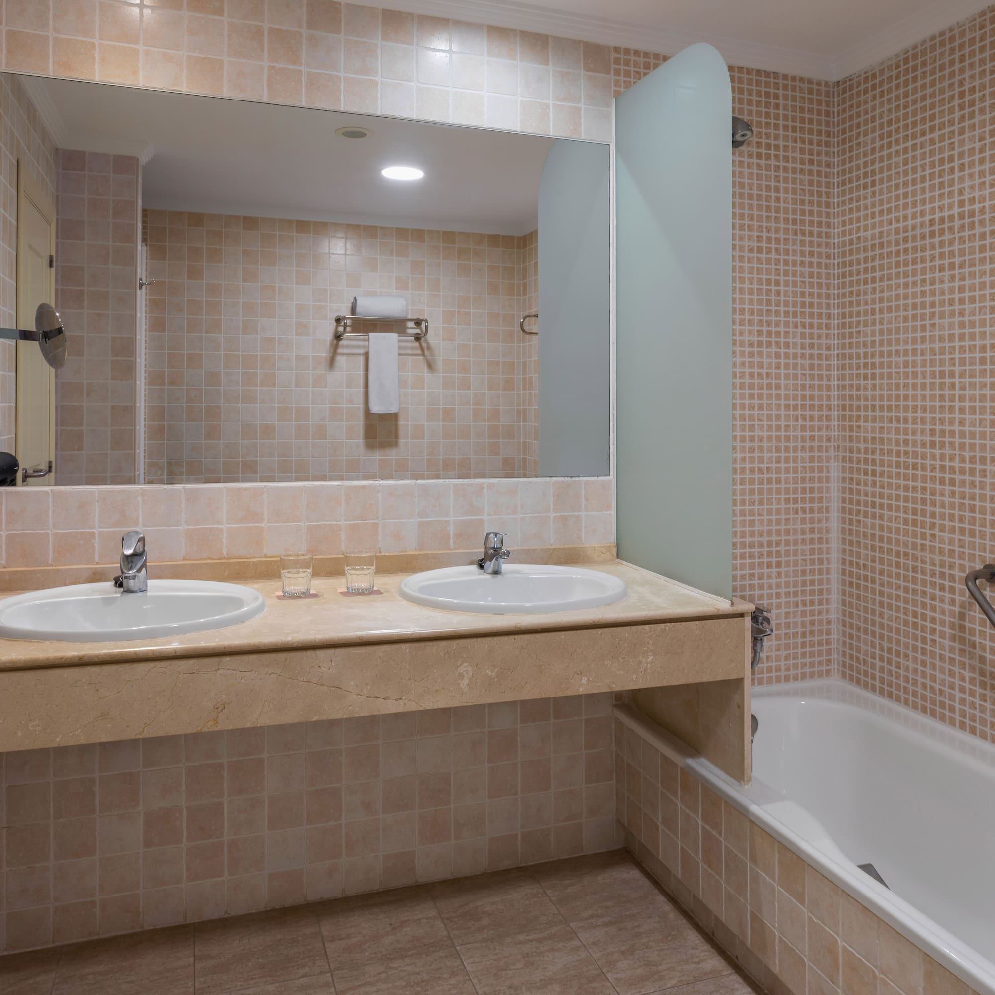 Clean tiled bathroom with double sink vanity, large mirror, and bathtub.