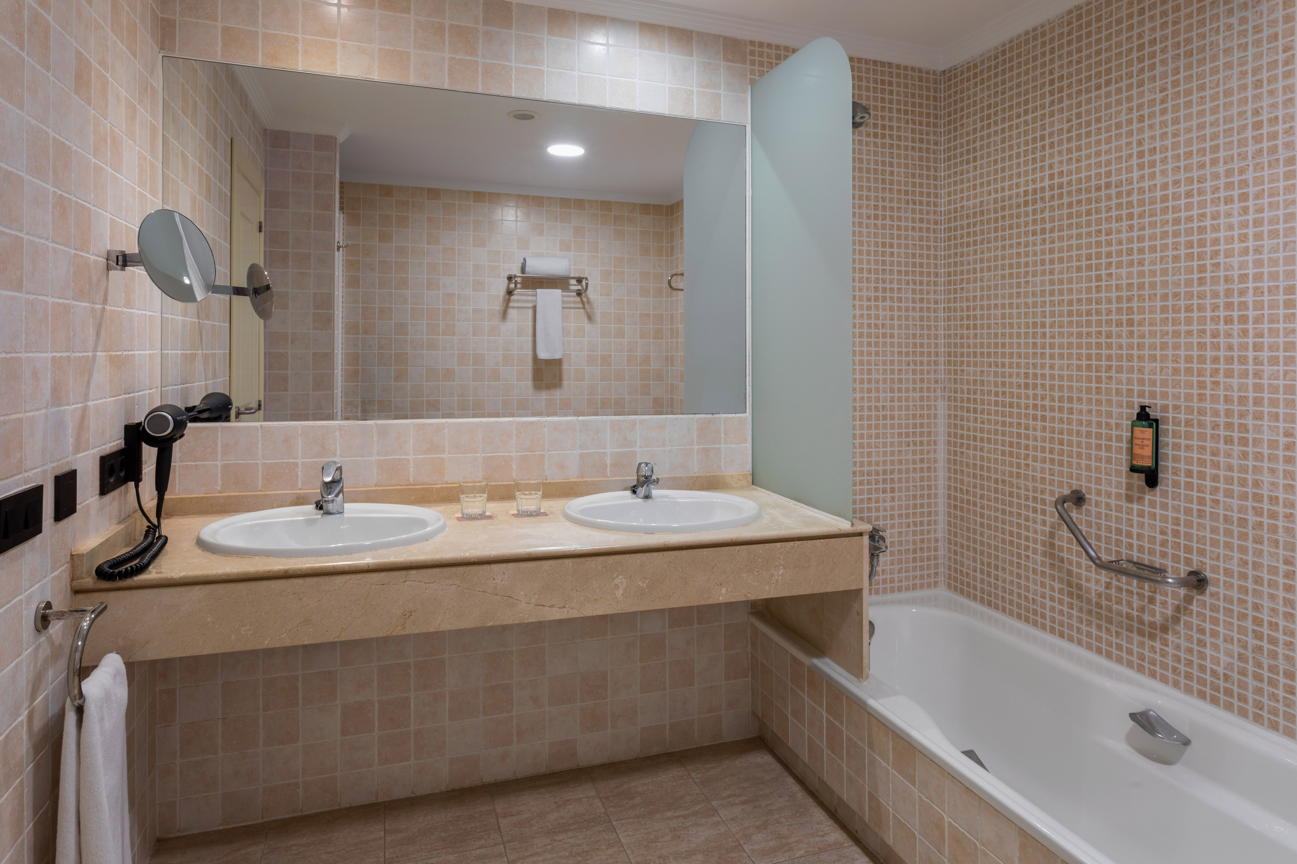 Clean tiled bathroom with double sink vanity, large mirror, and bathtub.