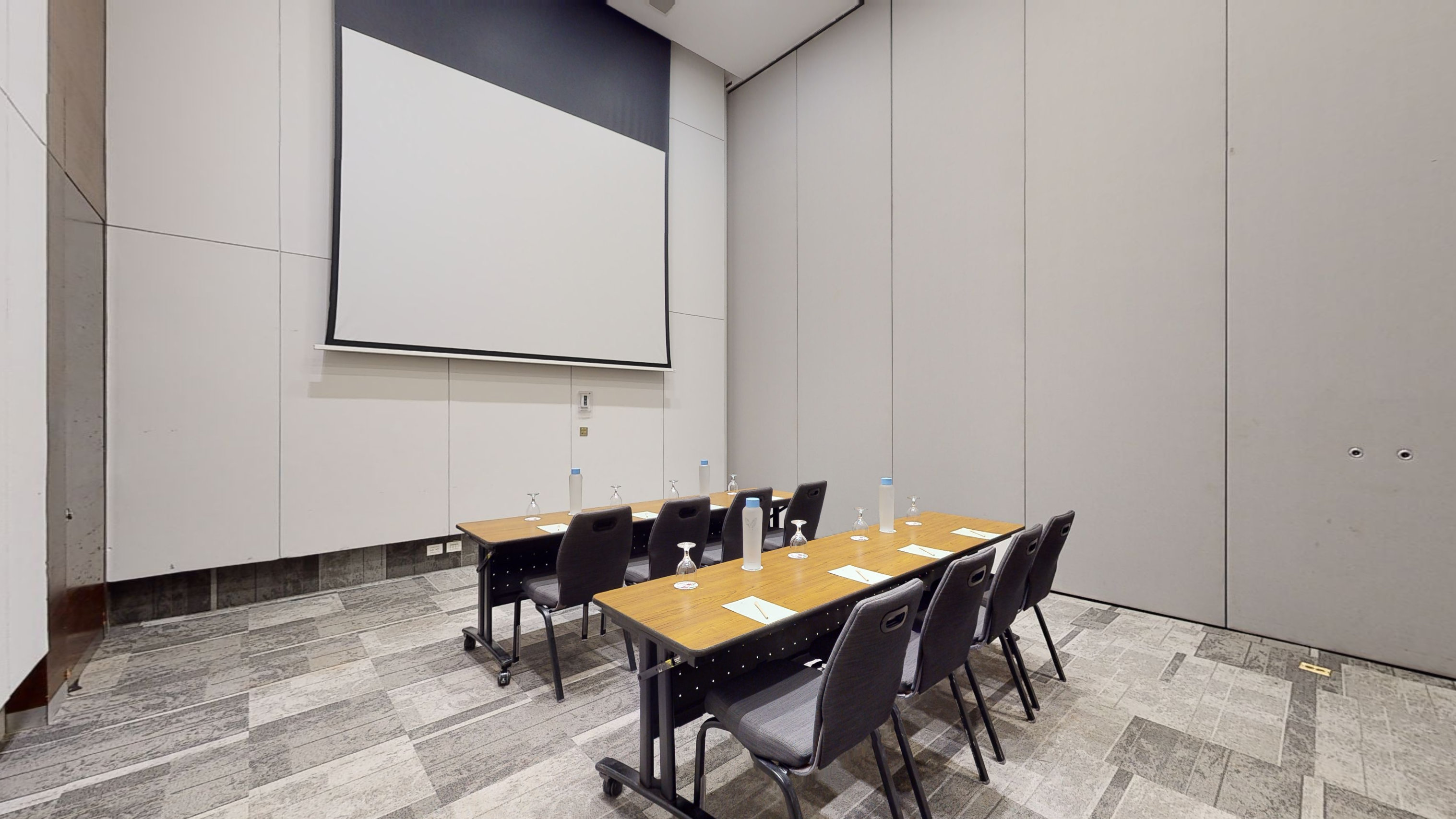 Modern conference room with projector screen, tables, chairs, and water bottles.