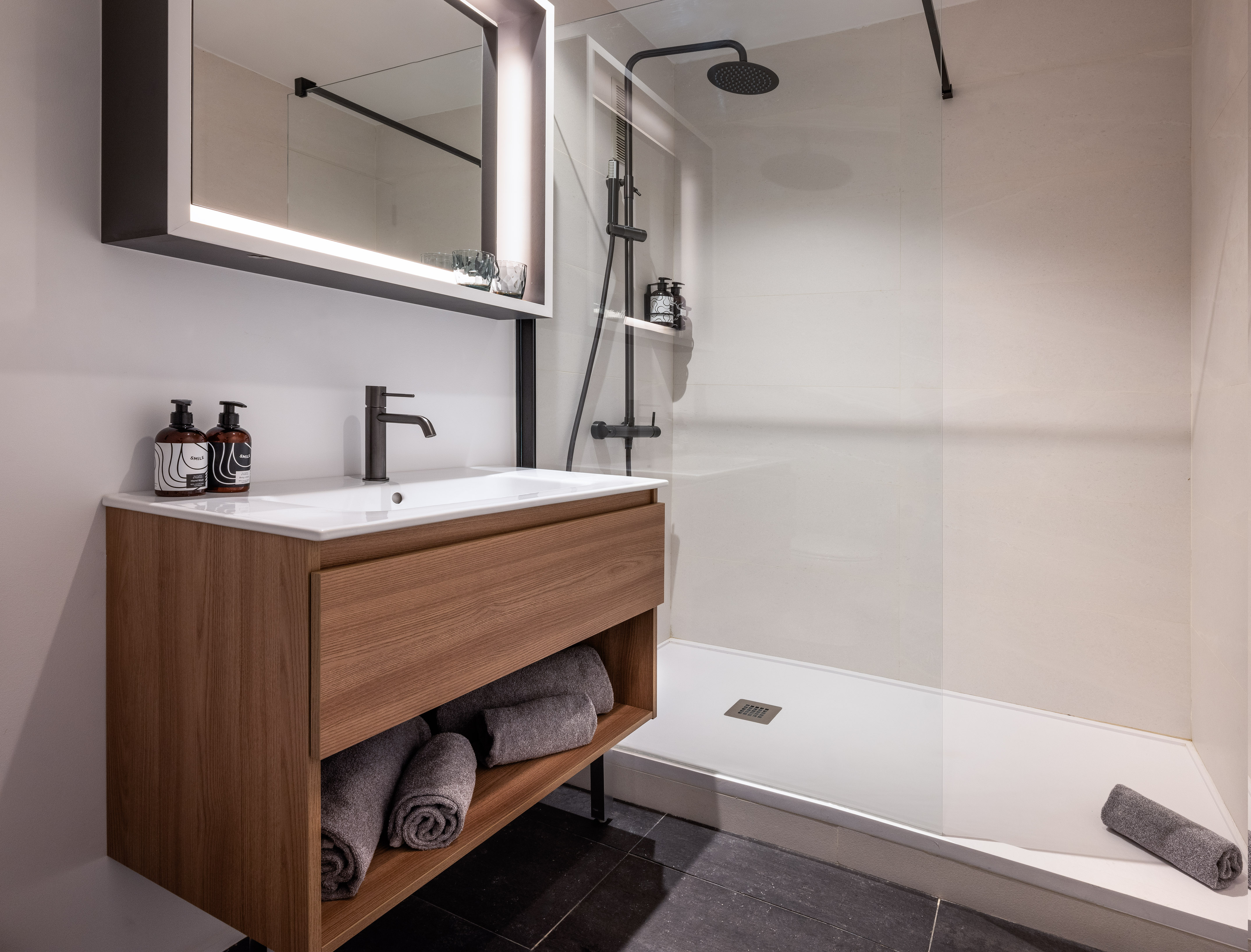 Modern bathroom with wooden vanity, backlit mirror, and glass walk-in shower.