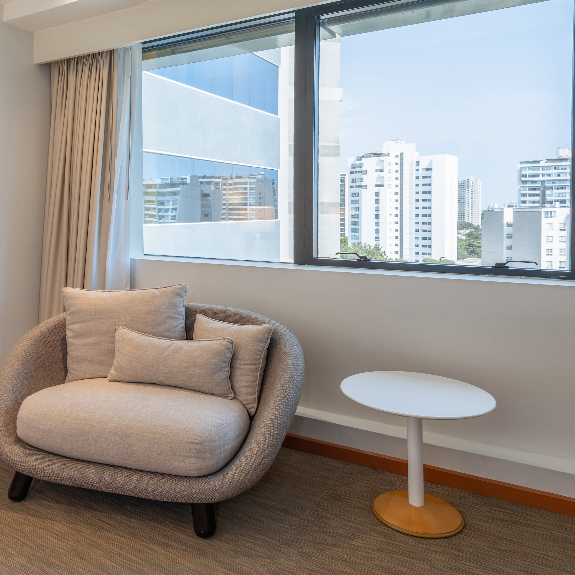 Interior moderno con sillón, mesa auxiliar y ventana con vistas urbanas.