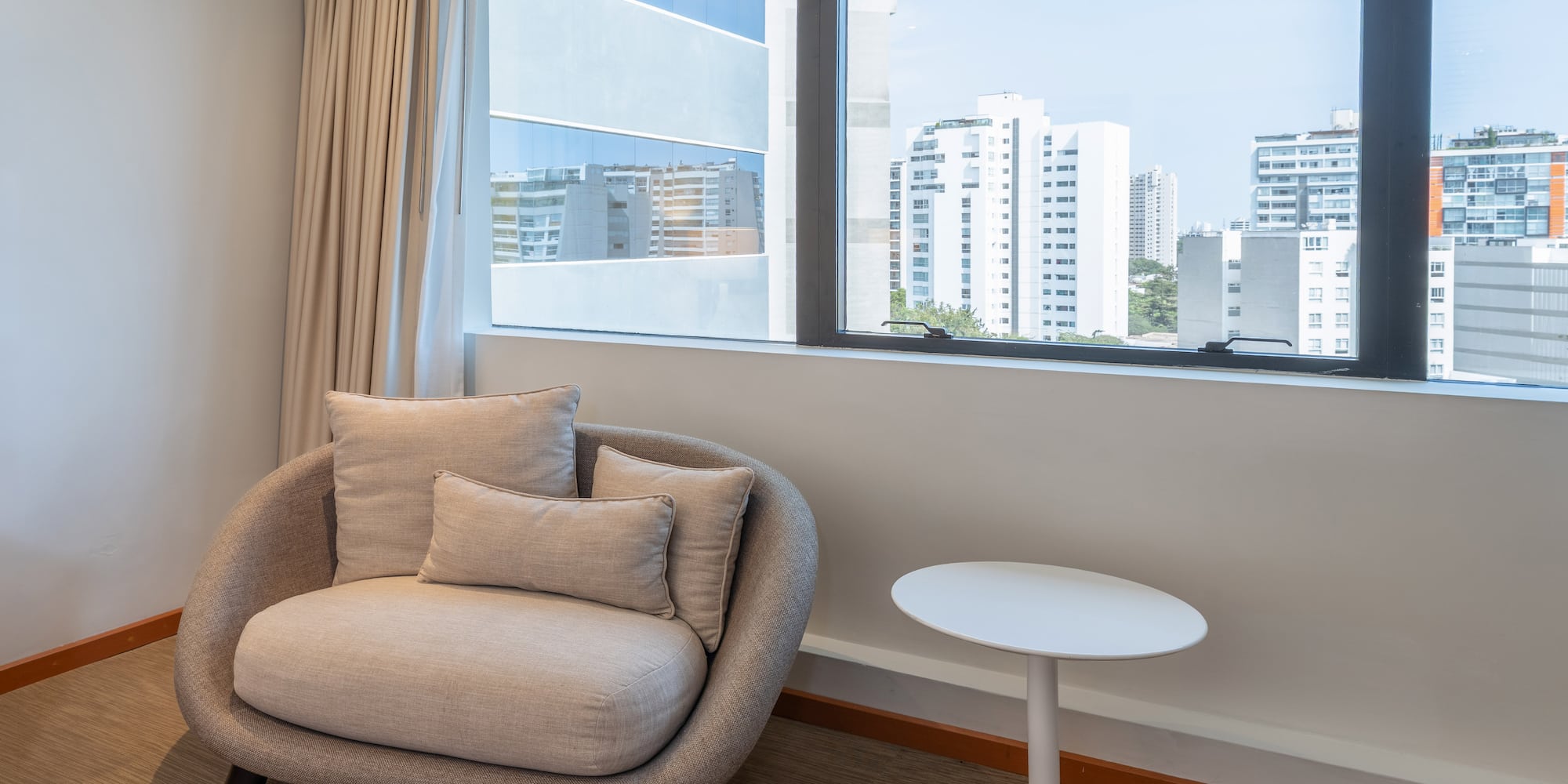 Interior moderno con sillón, mesa auxiliar y ventana con vistas urbanas.