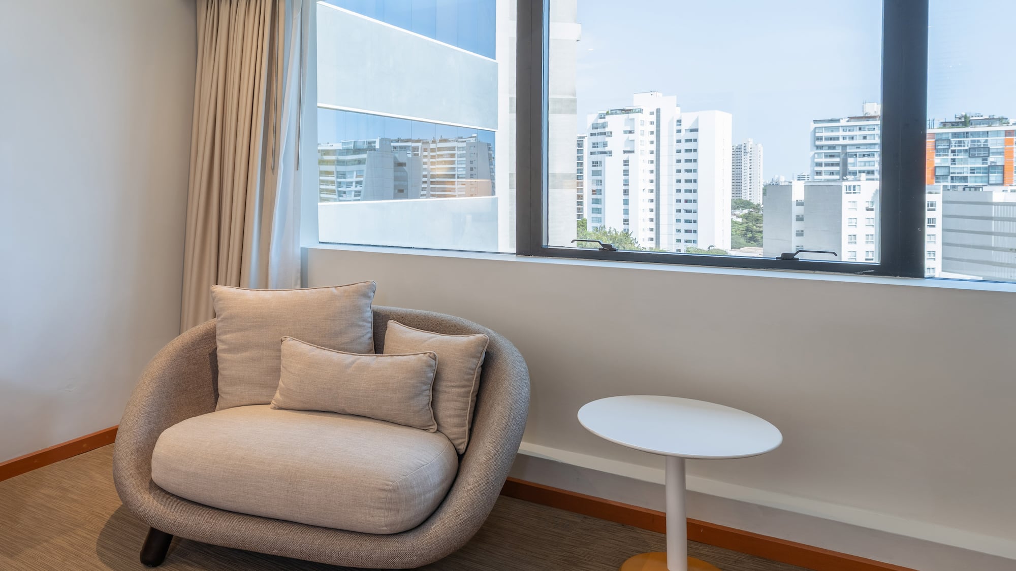 Interior moderno con sillón, mesa auxiliar y ventana con vistas urbanas.
