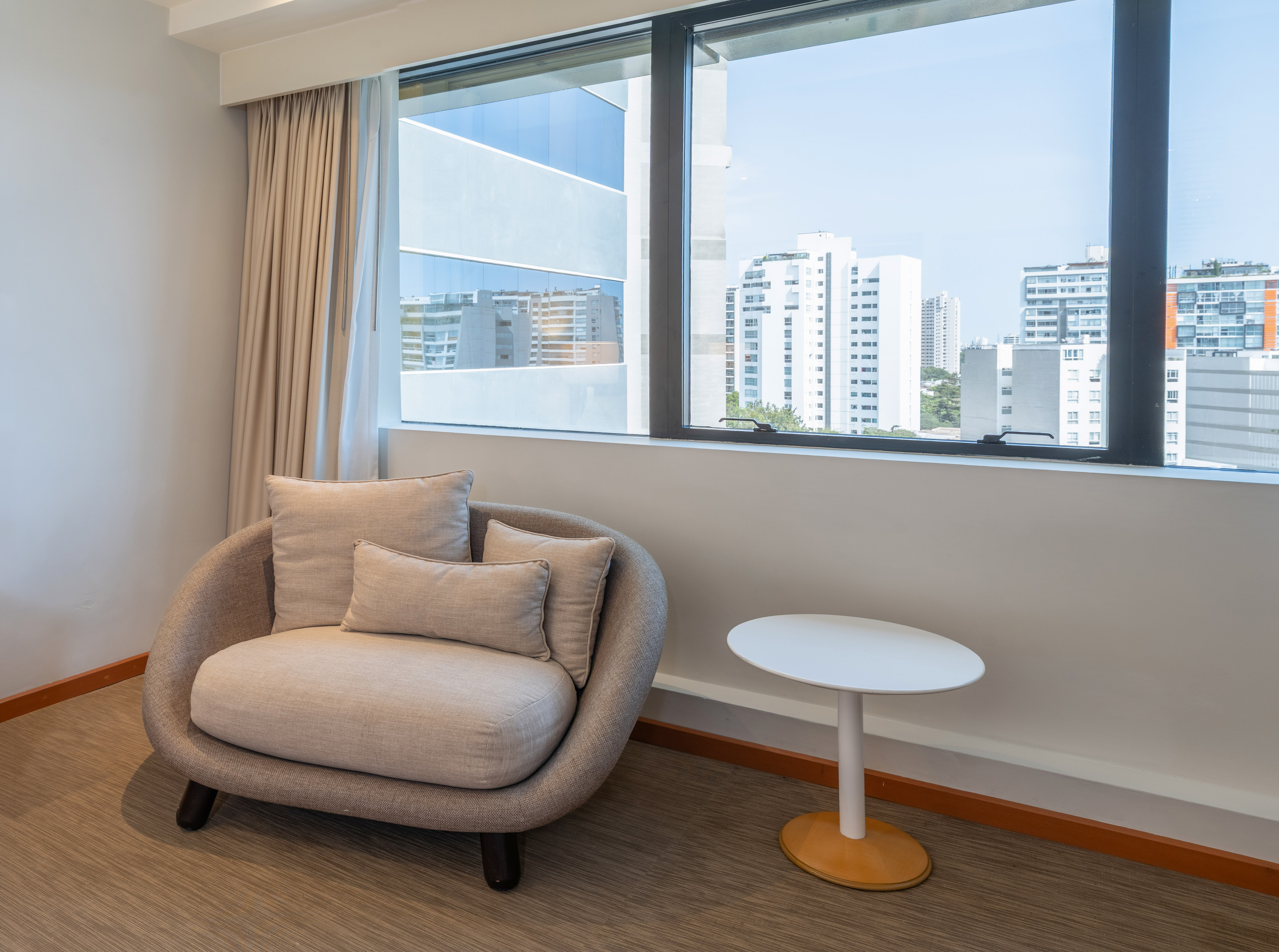 Interior moderno con sillón, mesa auxiliar y ventana con vistas urbanas.