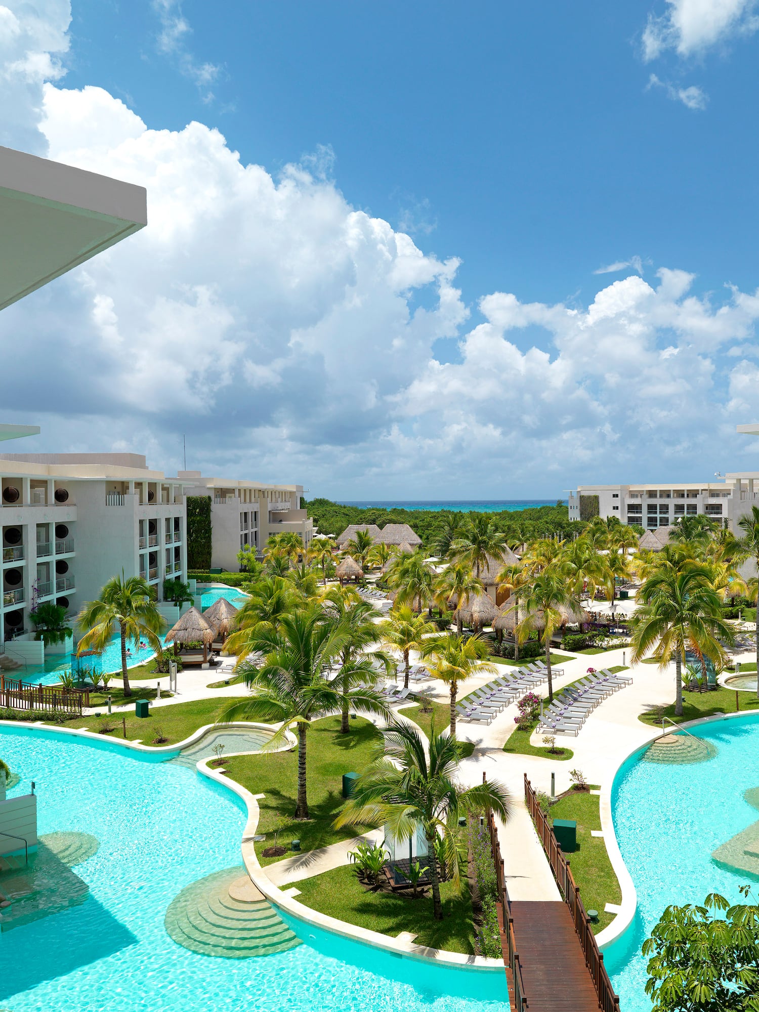 Resort with lagoon pools, palm trees, white buildings, distant ocean.