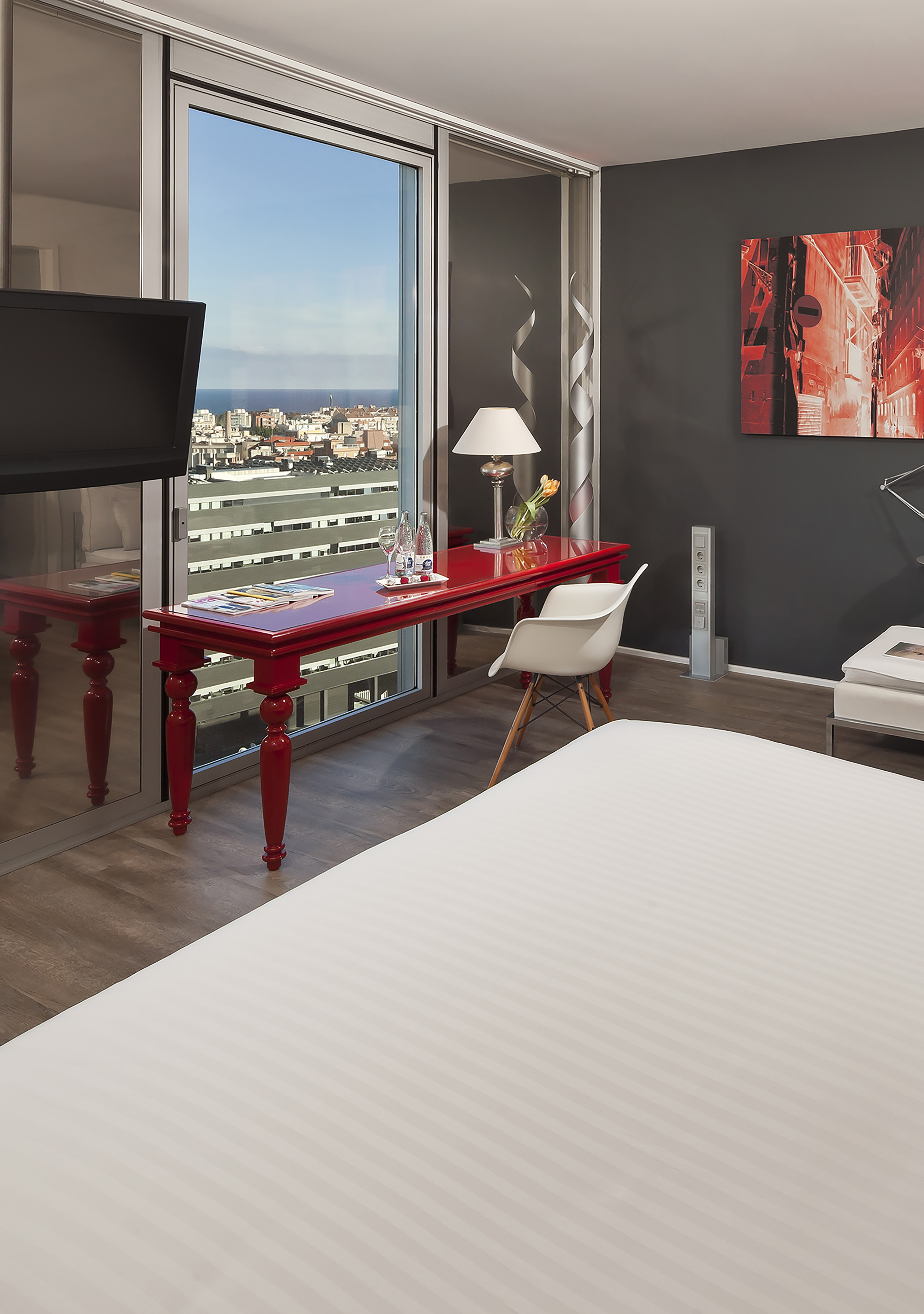 Modern hotel room with red desk, panoramic city and sea view.