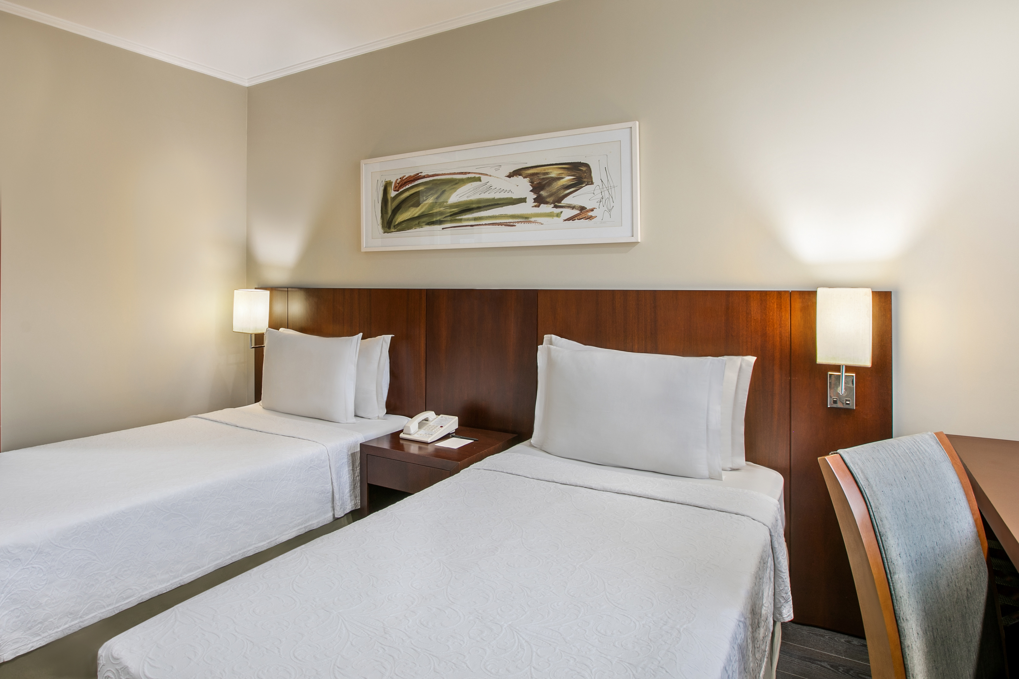 Modern hotel guest room with two twin beds, bedside lamps, and abstract artwork.