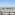 Elevated view of white villas, palm trees, and mountains against a clear sky.
