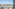 Elevated view of white villas, palm trees, and mountains against a clear sky.
